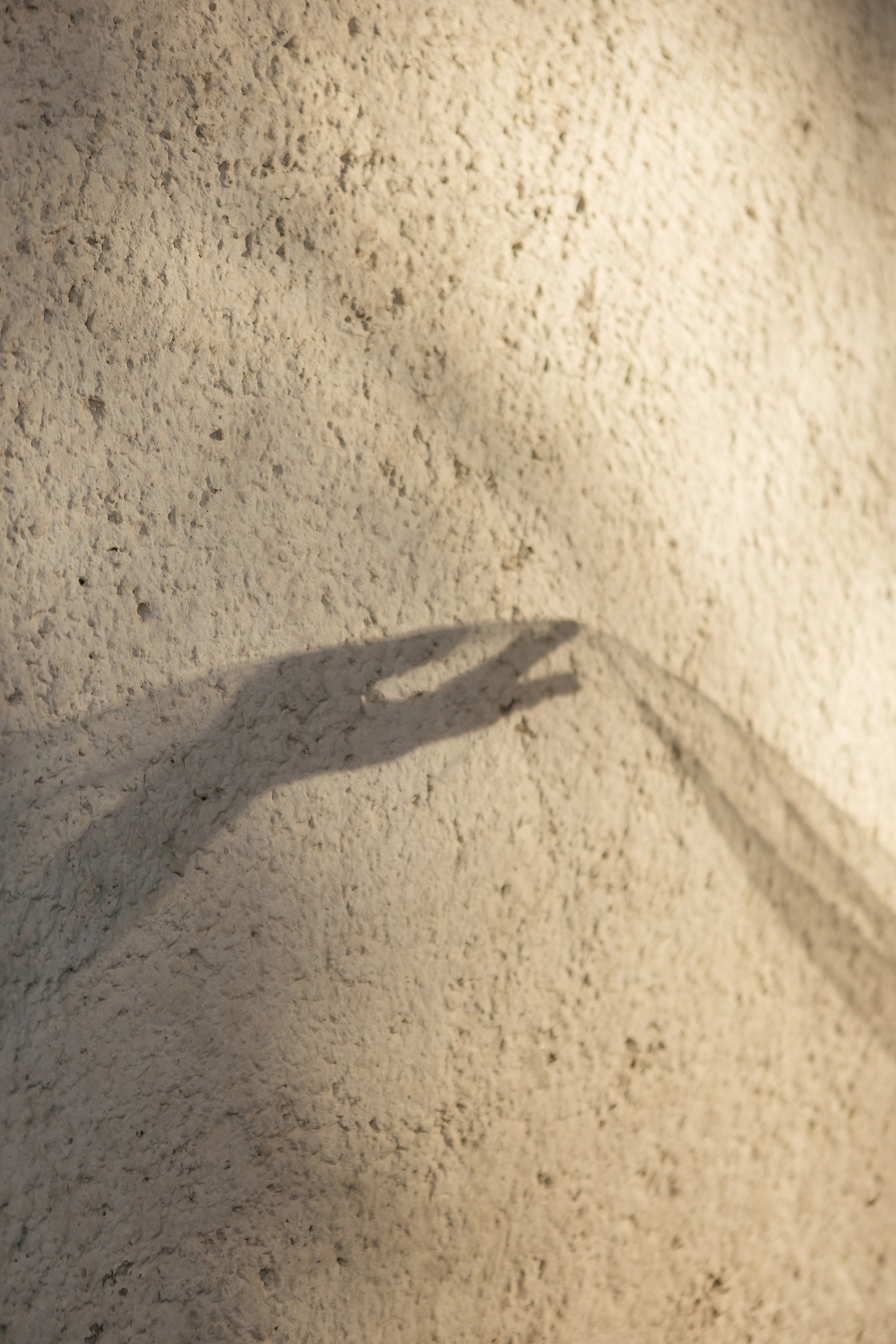 тень руки и ткани на фактурной стене в тёплом закатном свете