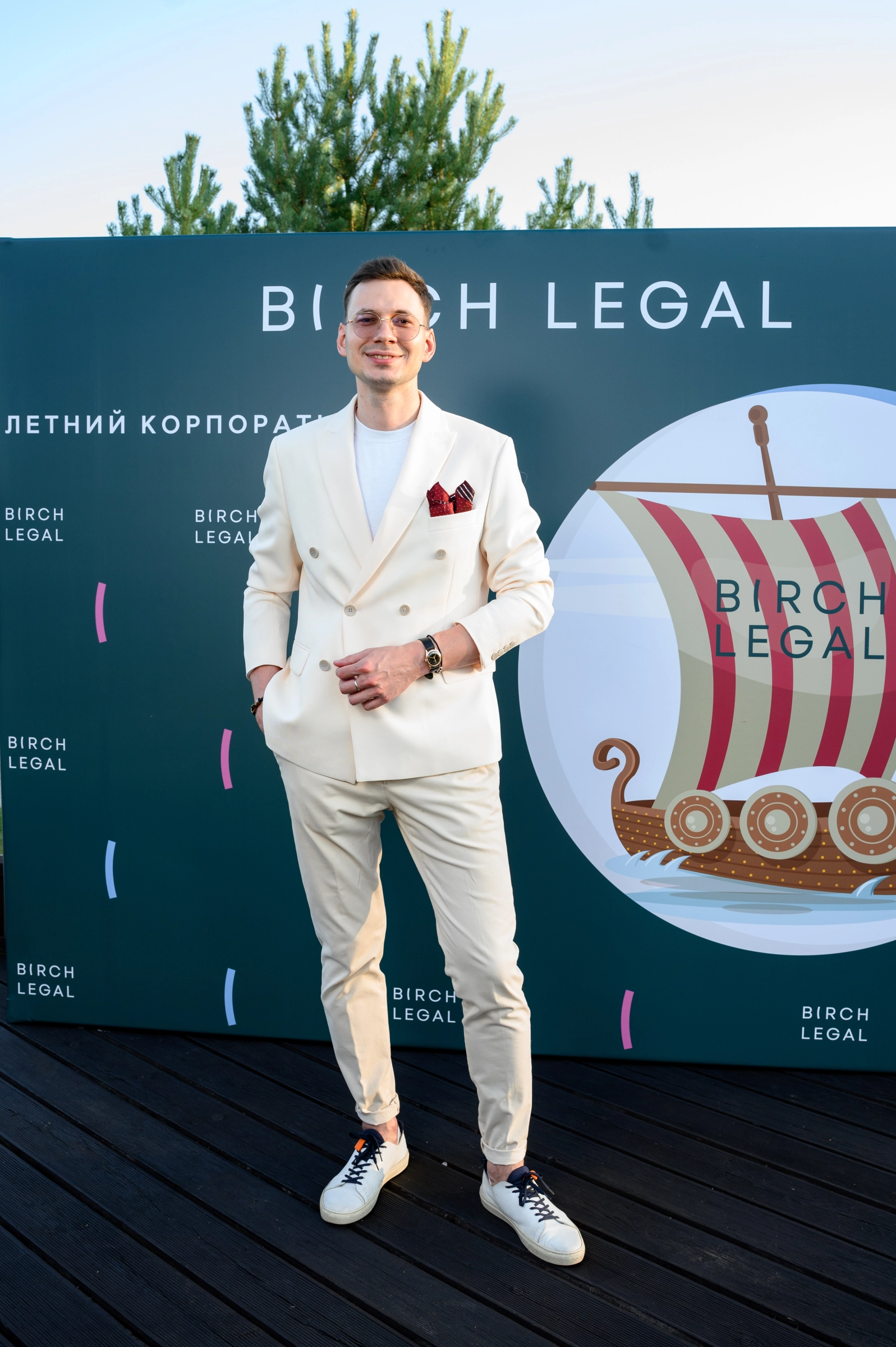 ведущий в кремовом костюме на фоне корпоративного стенда