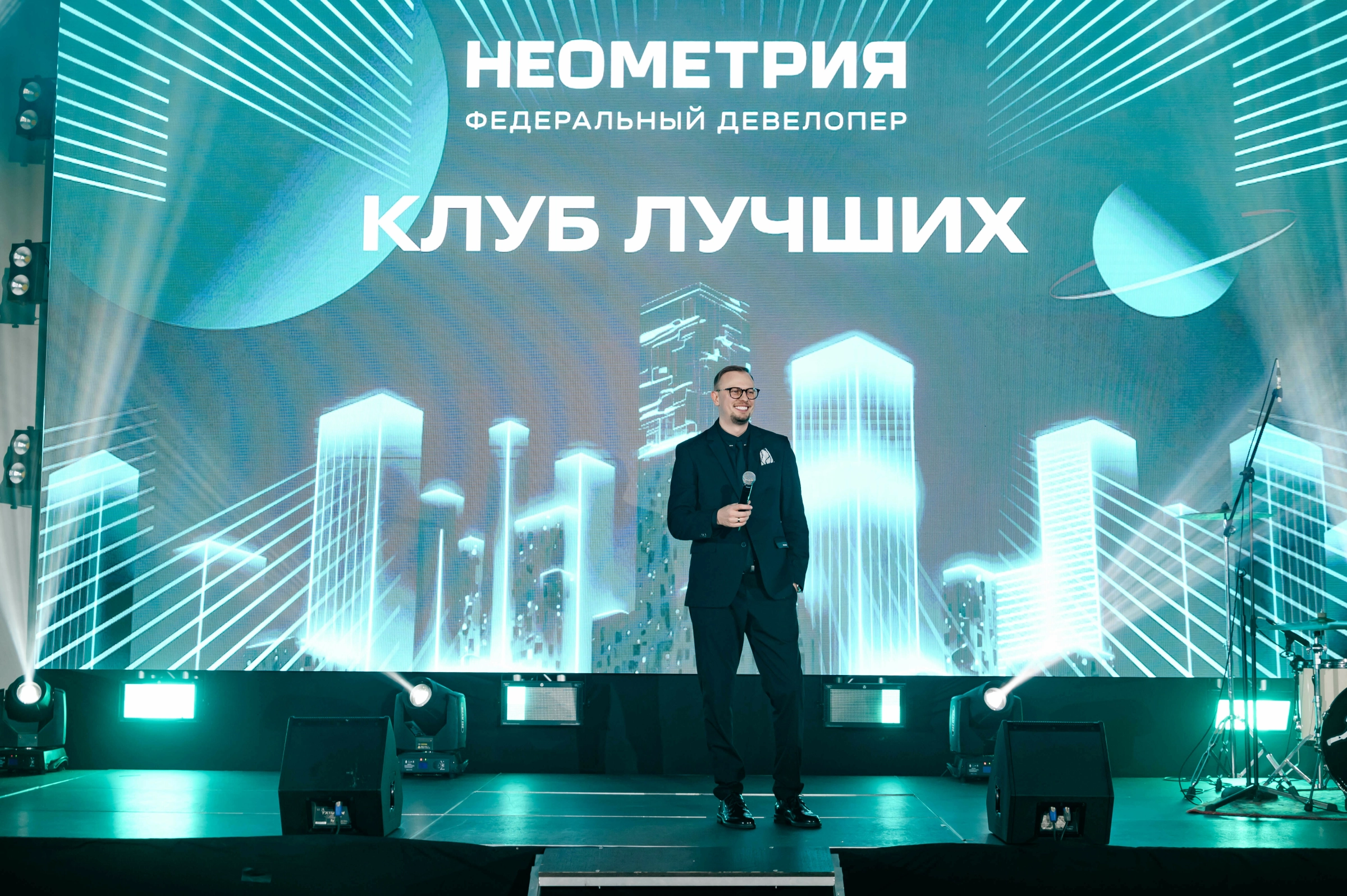 Ведущий с микрофоном выступает на сцене корпоративного мероприятия