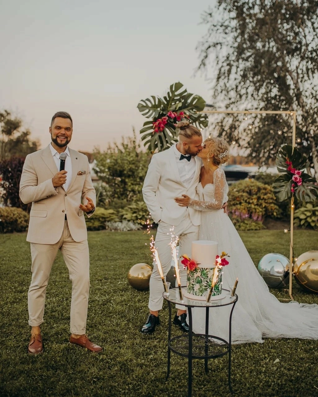 ведущий с микрофоном на фоне целующихся жениха и невесты