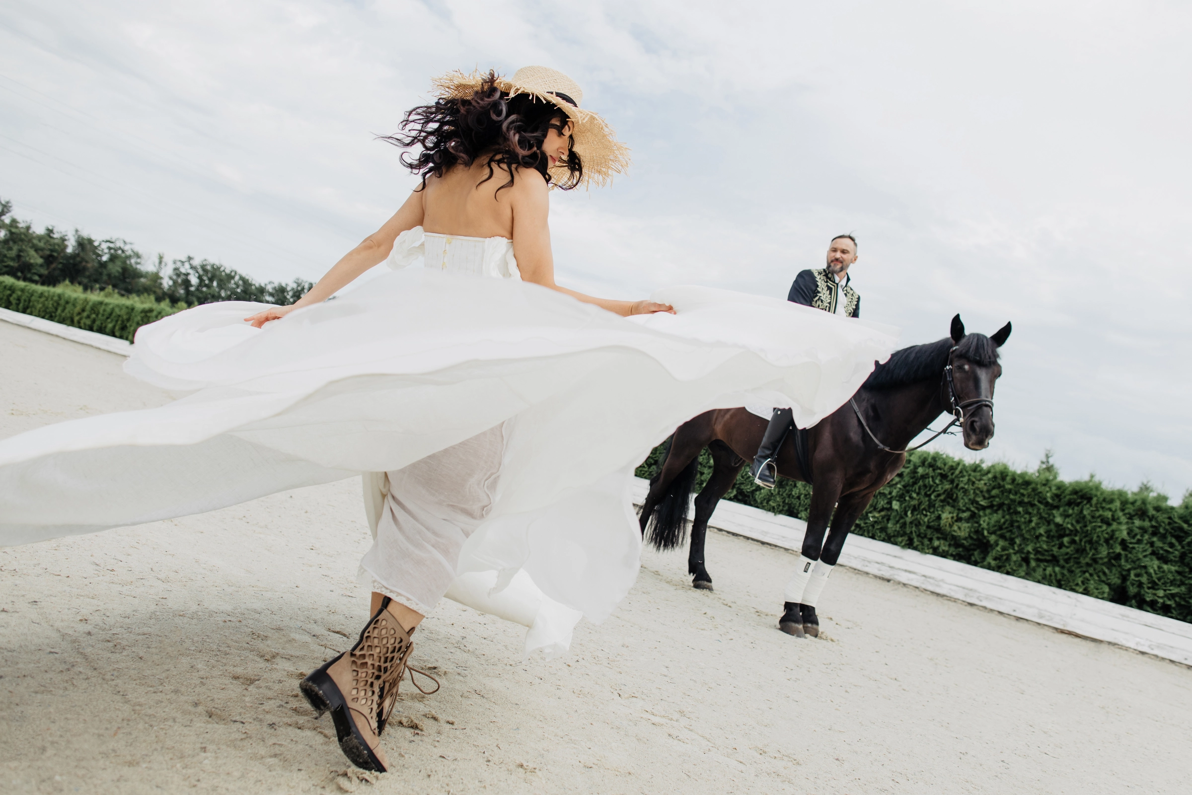 невеста в шляпе бежит по манежу, жених едет верхом позади