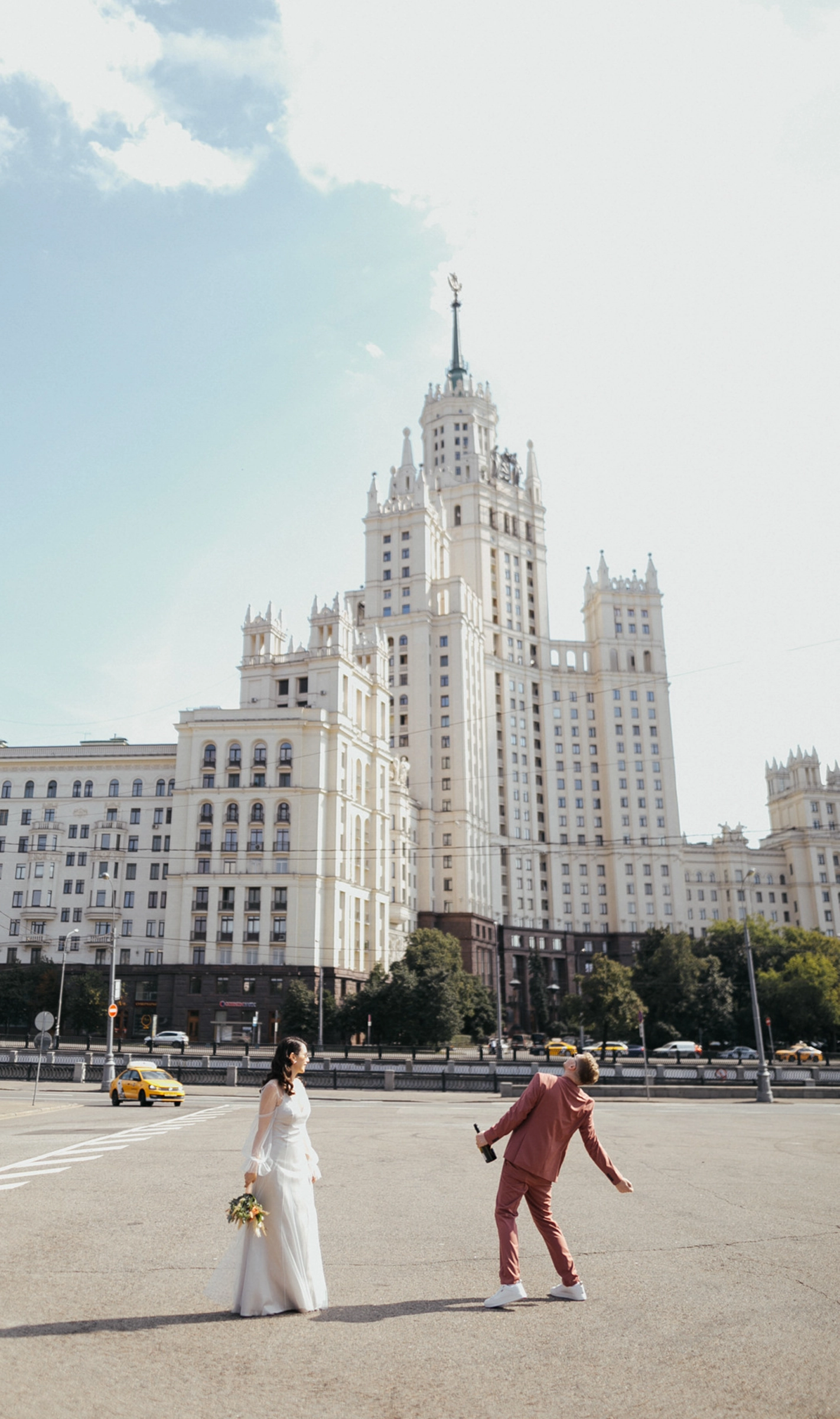 Жених и невеста идут по площади на фоне высотного здания