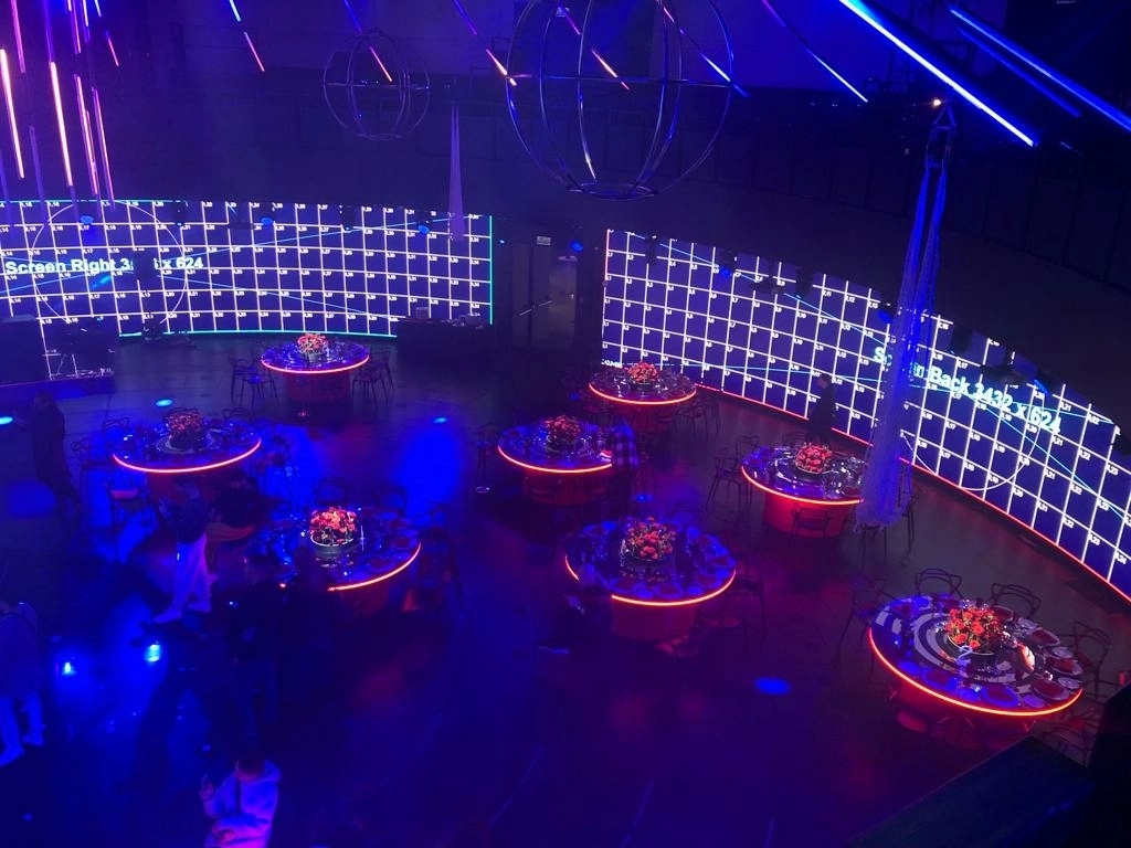 Круглые столы с подсветкой на фоне синей LED-стены в банкетном зале