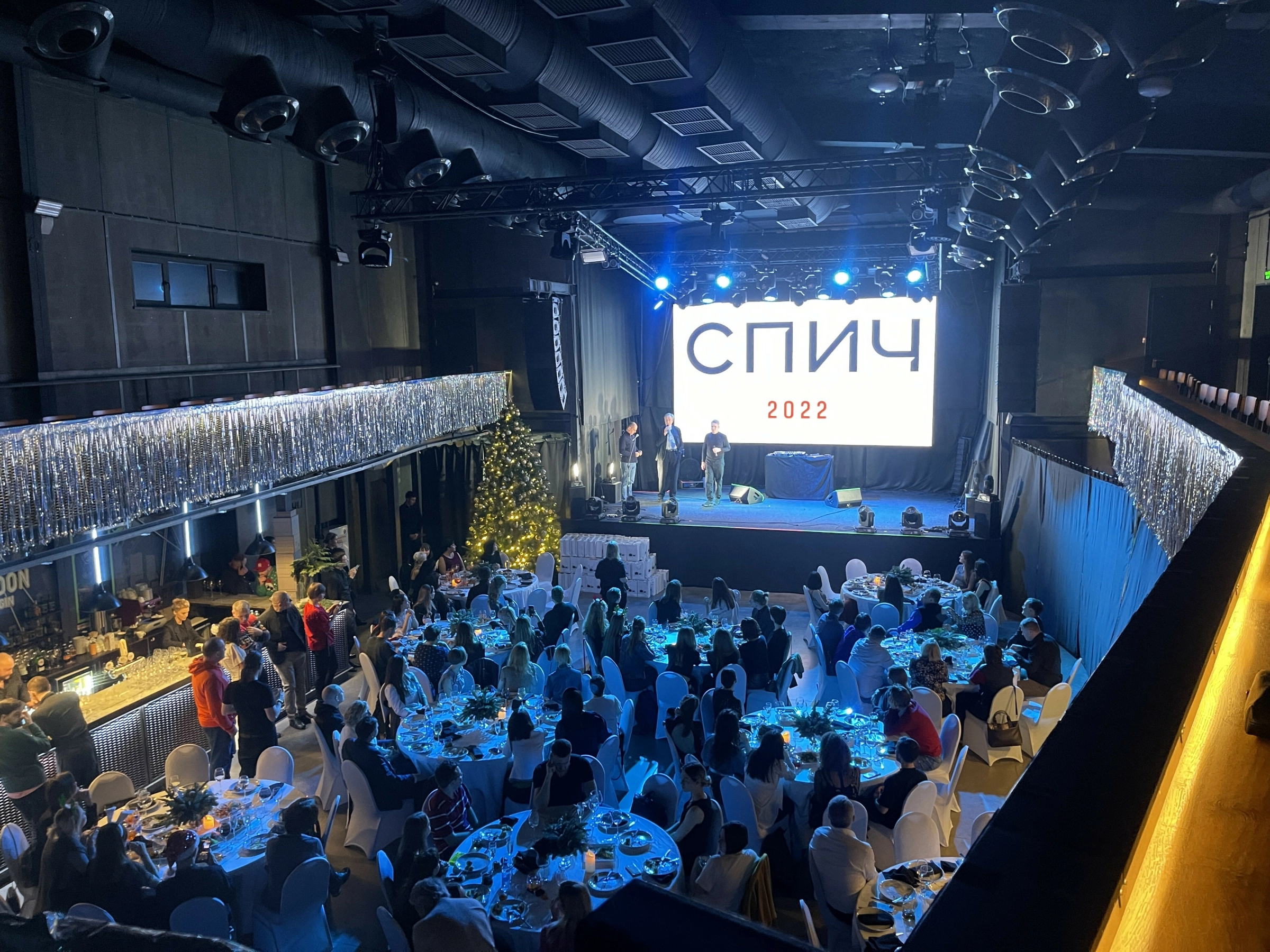 круглые столы гостей перед сценой с серебристым занавесом
