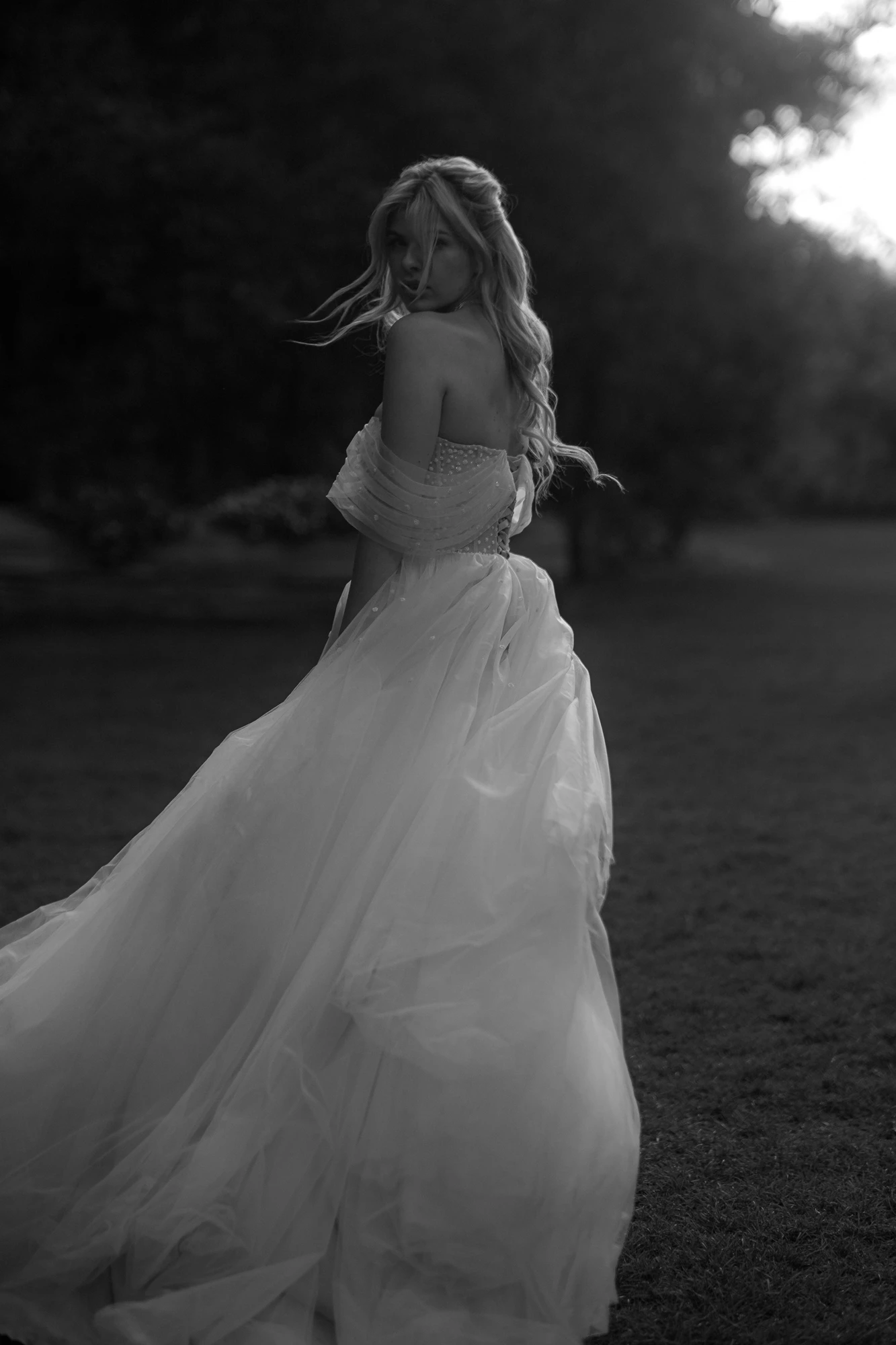 Невеста в пышном платье с открытыми плечами оборачивается в парке