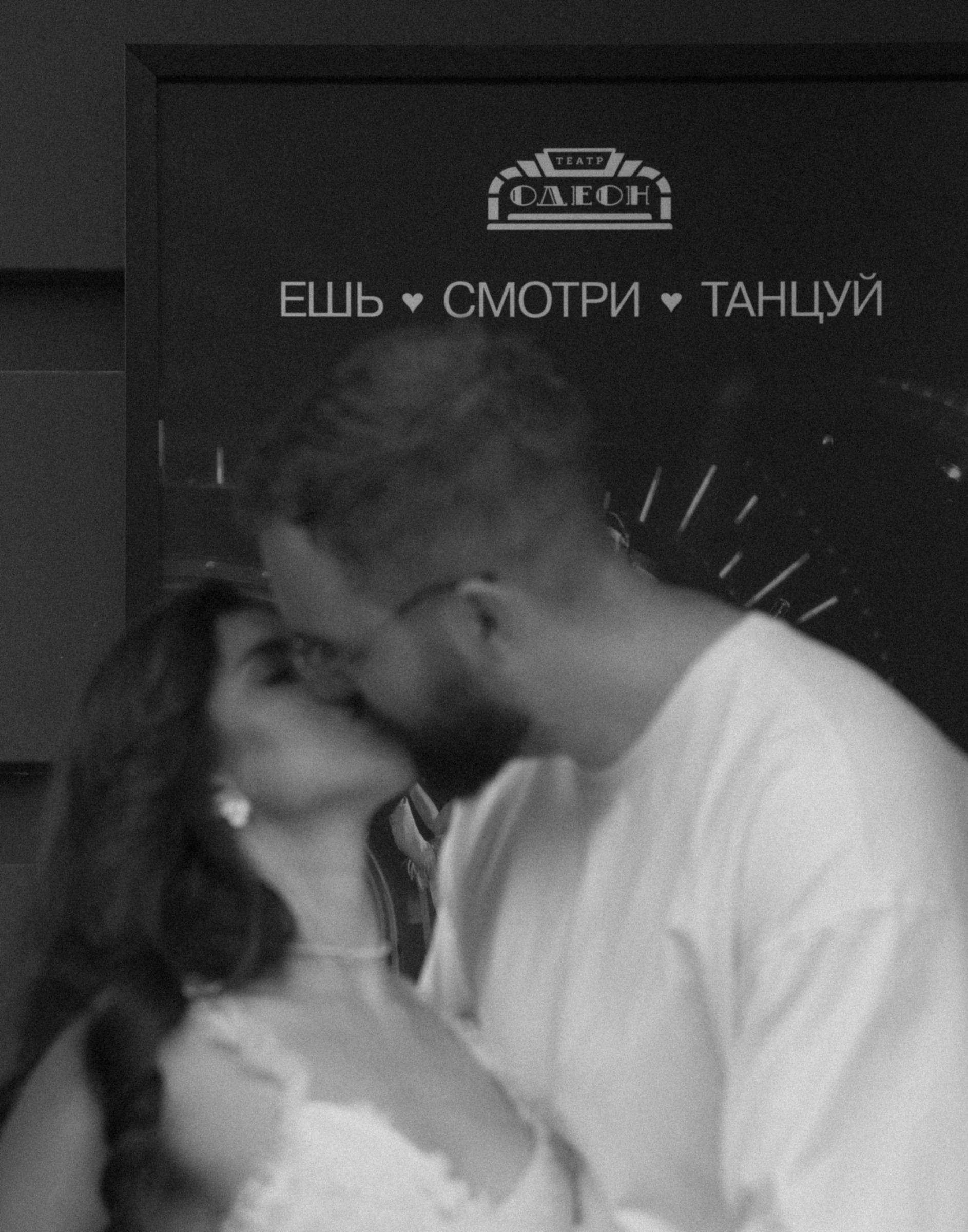 пара целуется на фоне тёмной театральной афиши в чёрно-белом кадре