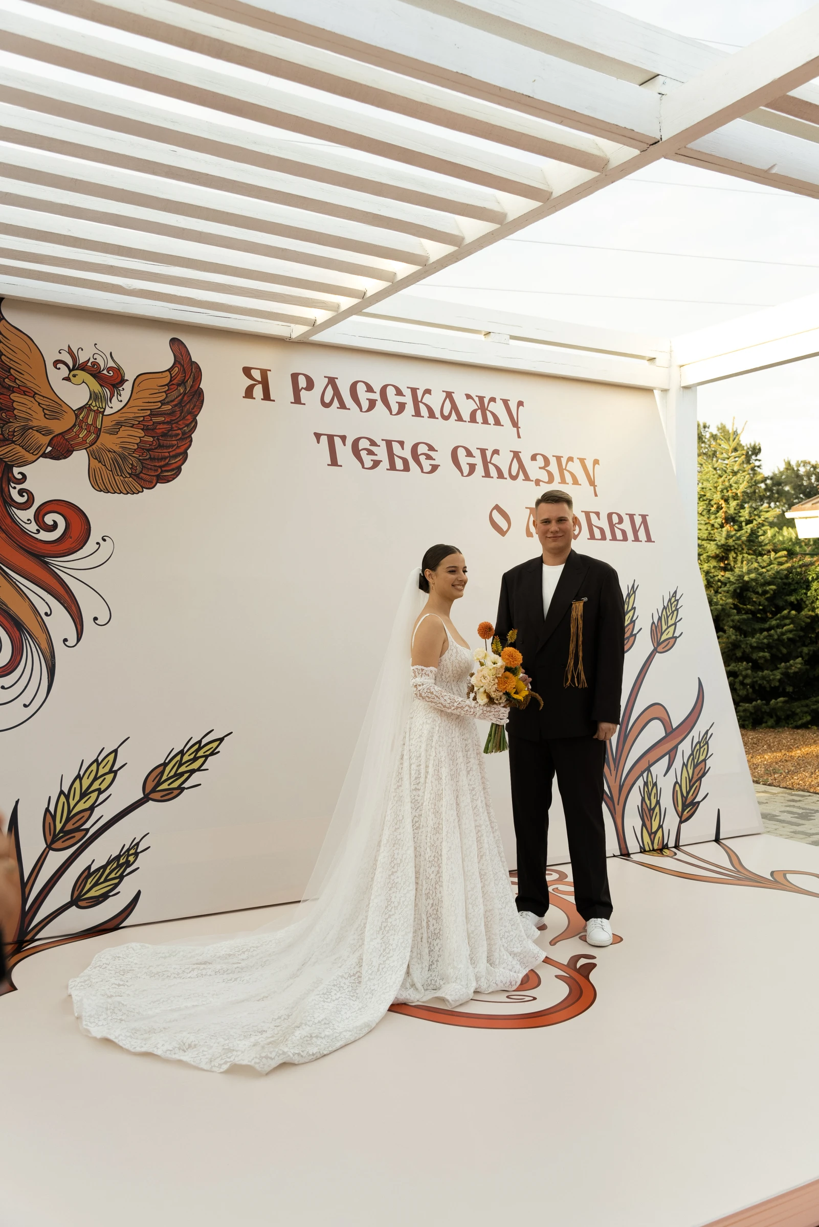 Пара позирует на сцене с яркой росписью жар-птицы и колосьев