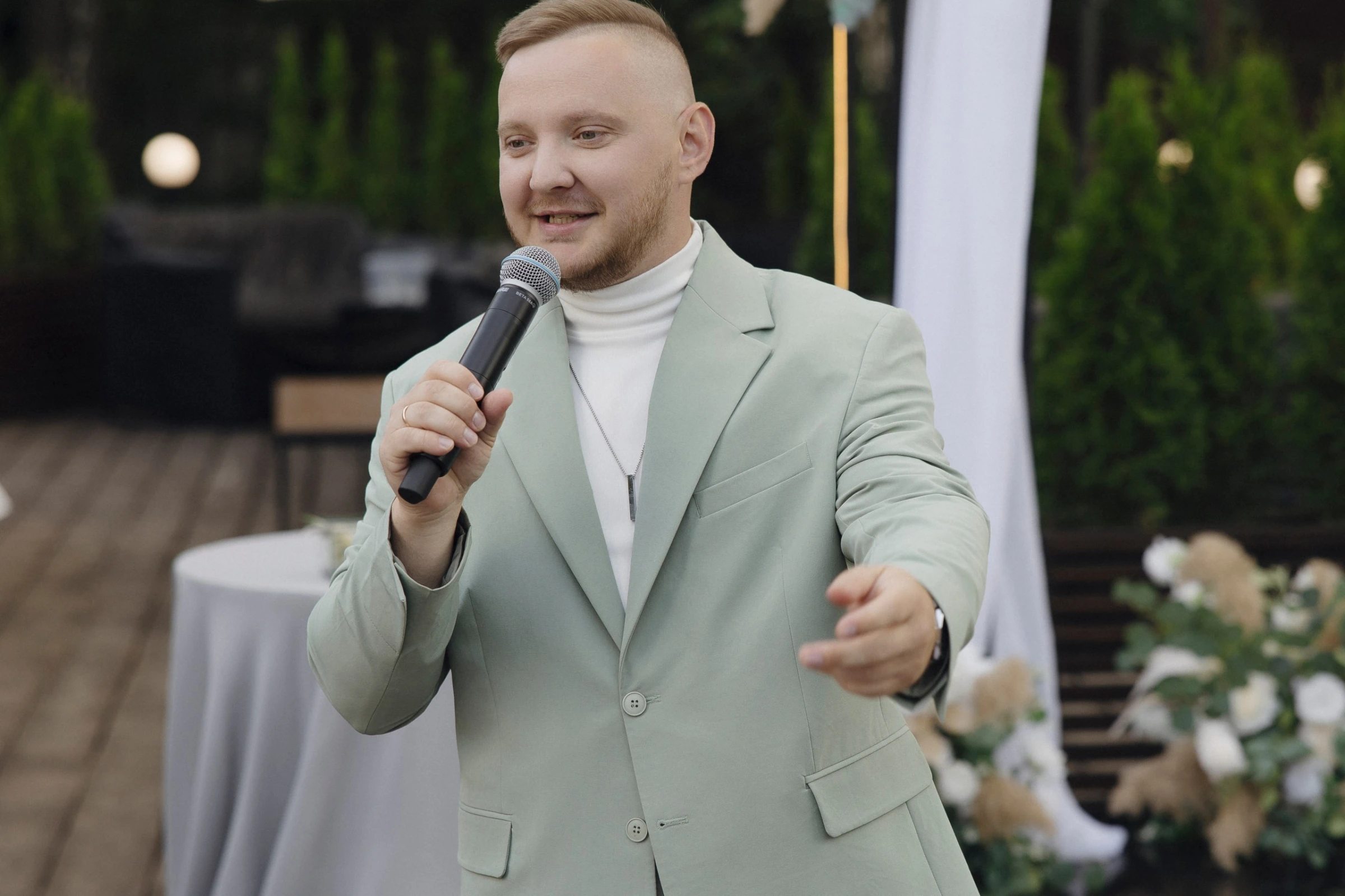 ведущий жестикулирует с микрофоном на озеленённой летней террасе
