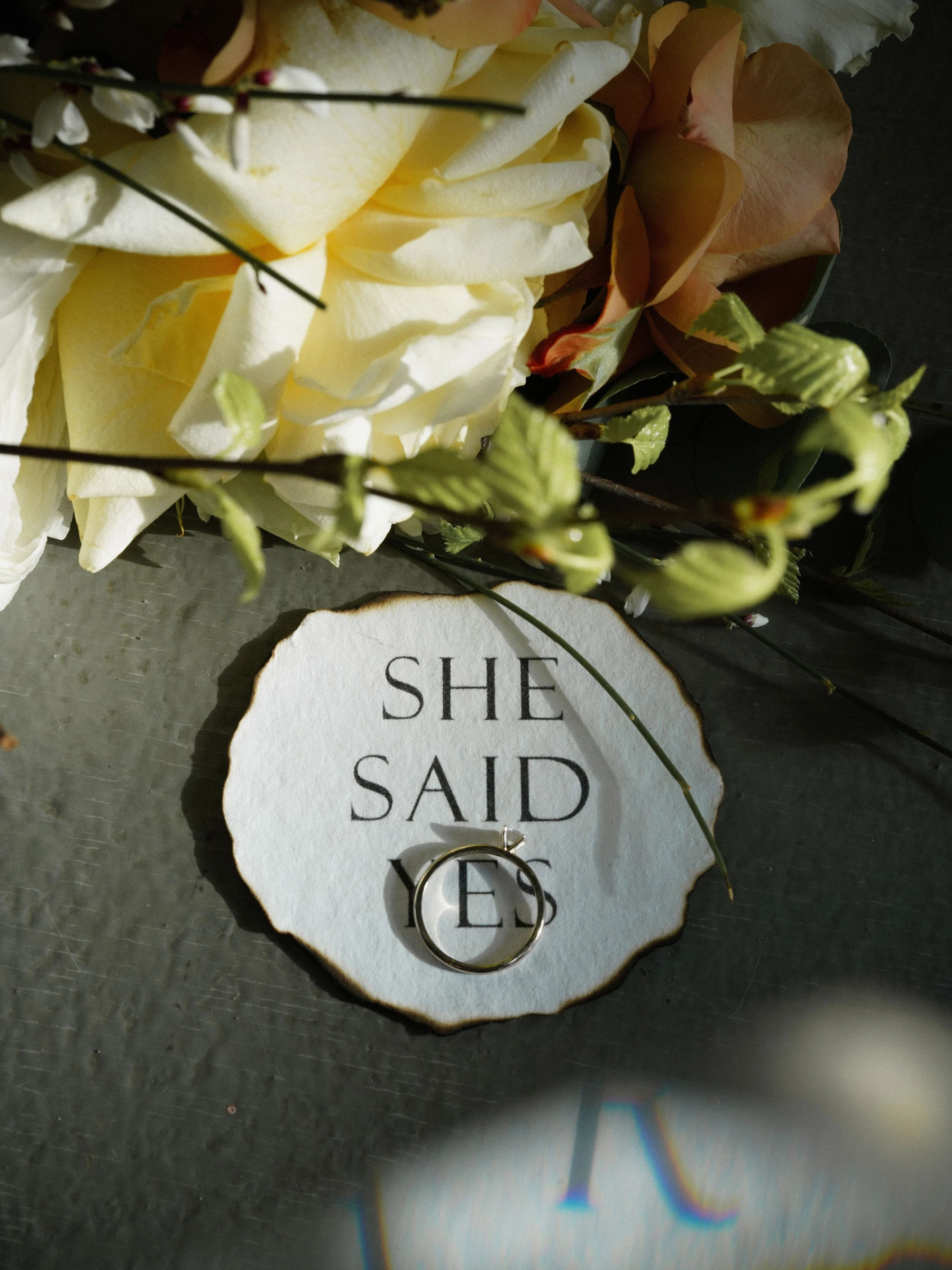 обручальное кольцо на табличке she said yes среди жёлтых и терракотовых роз