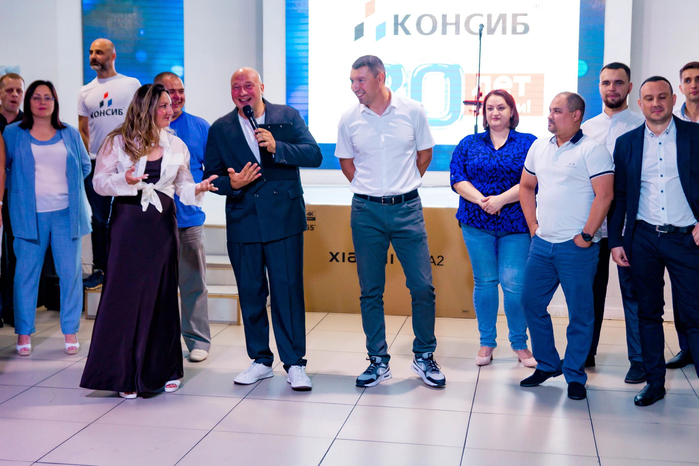 ведущий корпоратива с микрофоном общается с гостями на сцене в зале