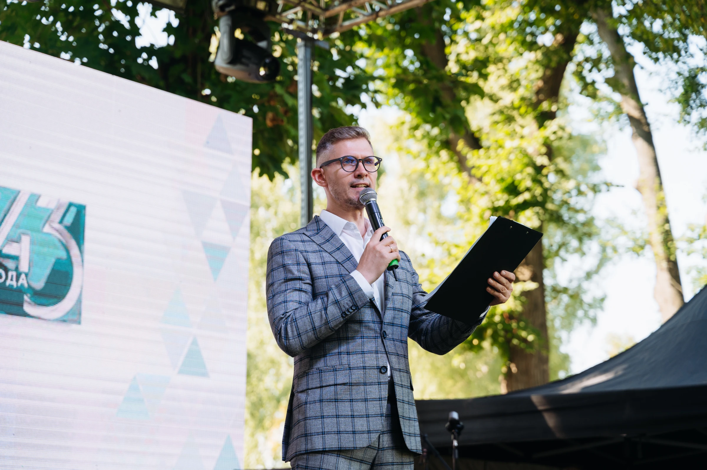 ведущий выступает с микрофоном на открытой сцене в парке