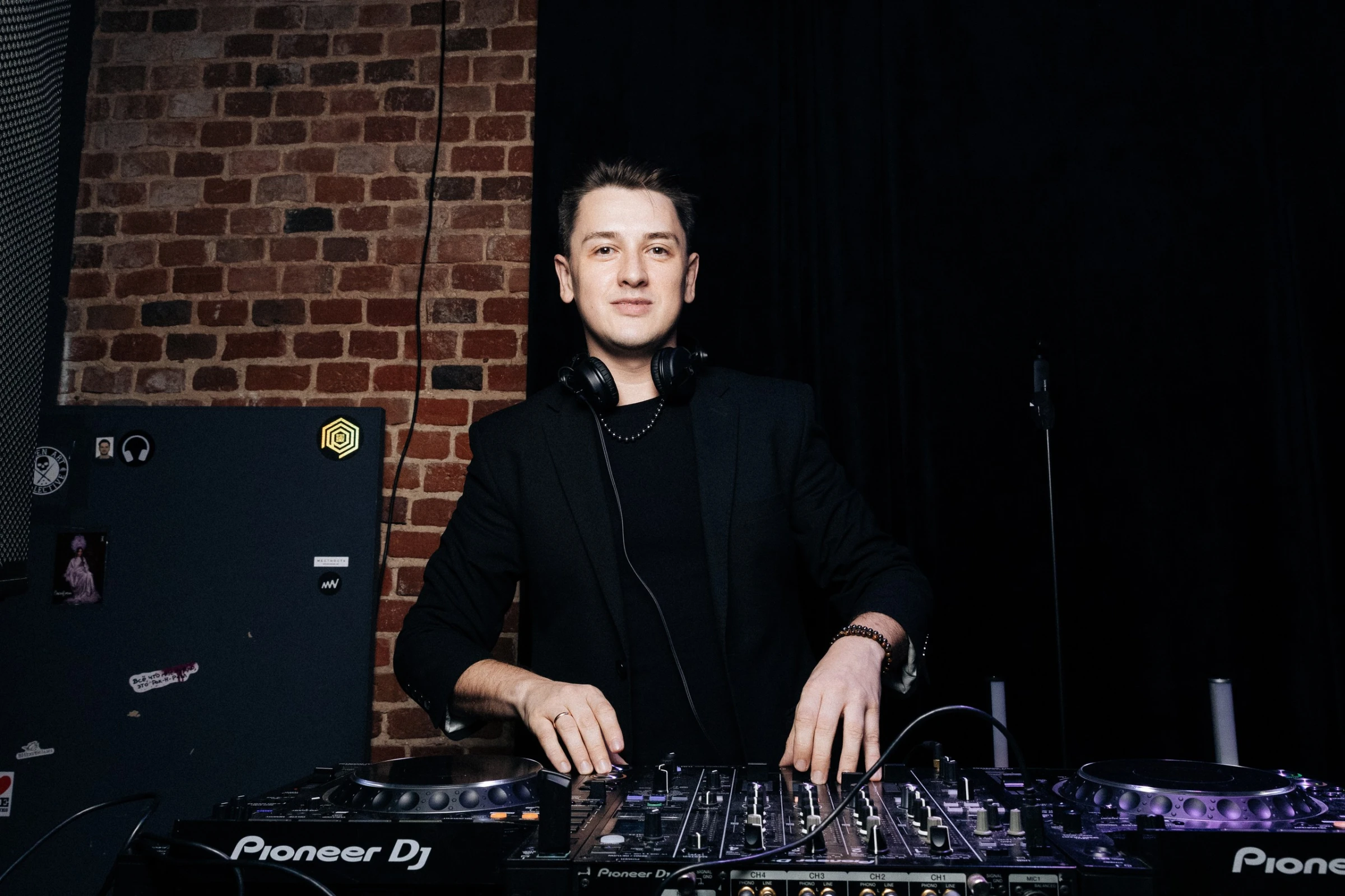 Диджей у пульта Pioneer на фоне кирпичной кладки в клубе