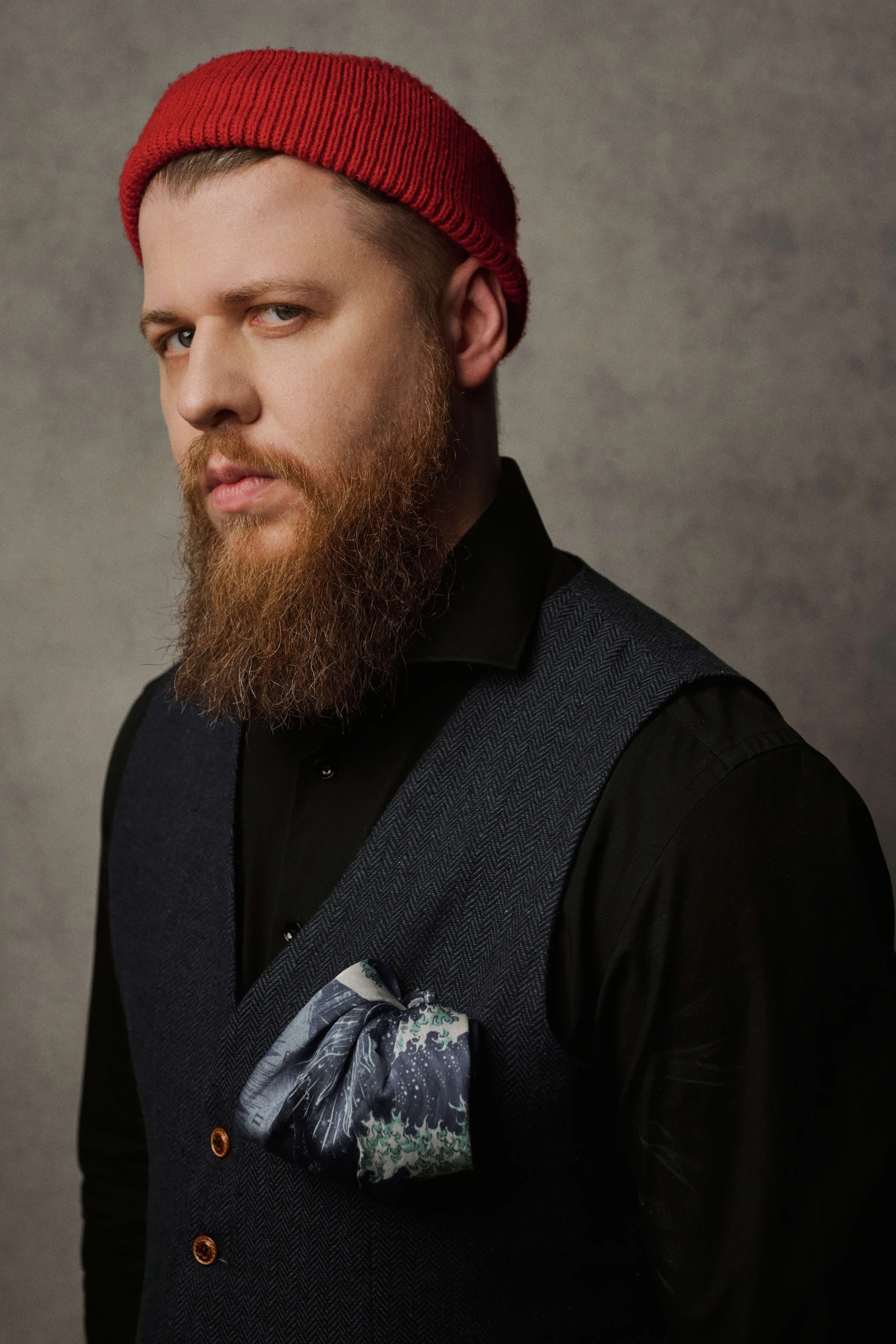 музыкант с рыжей бородой в красной вязаной шапке и жилете с платком