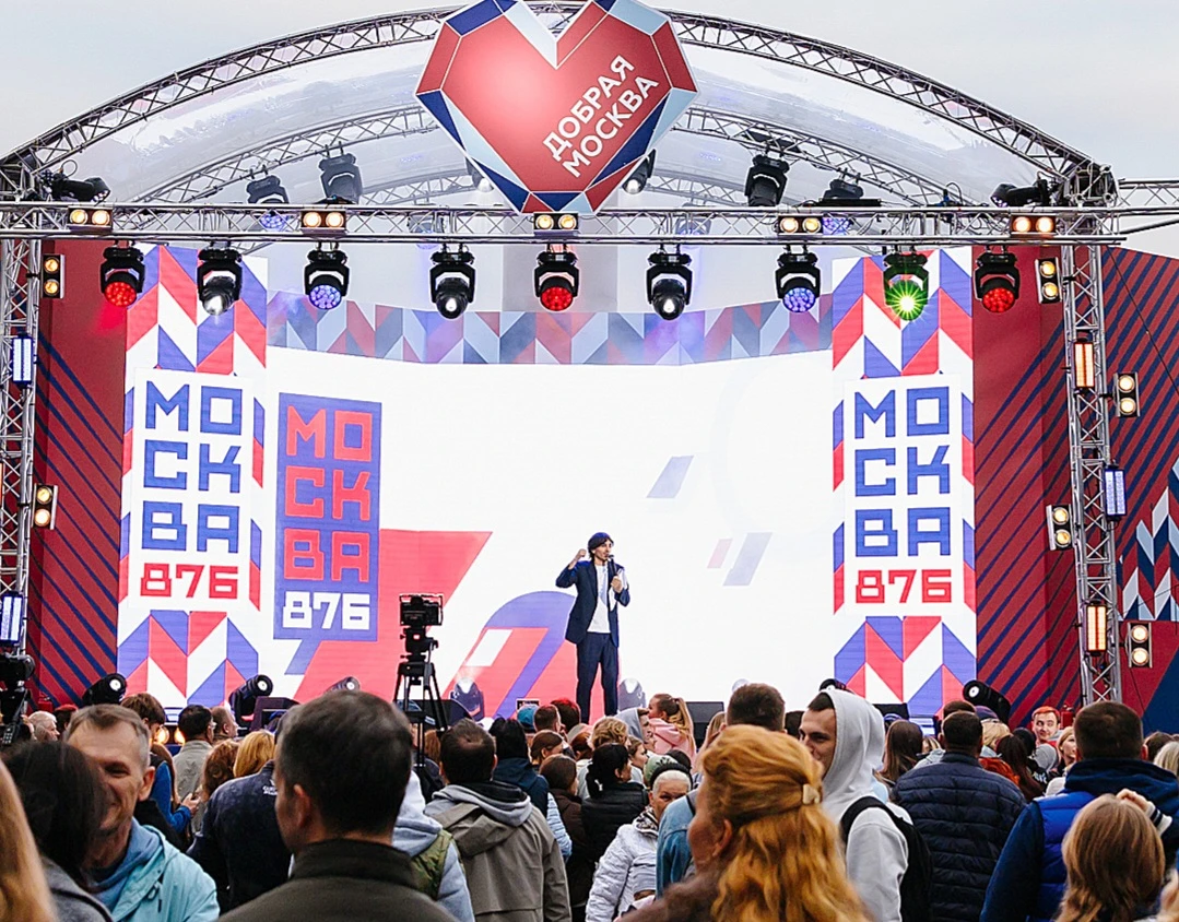мужчина с микрофоном выступает на сцене городского праздника перед толпой