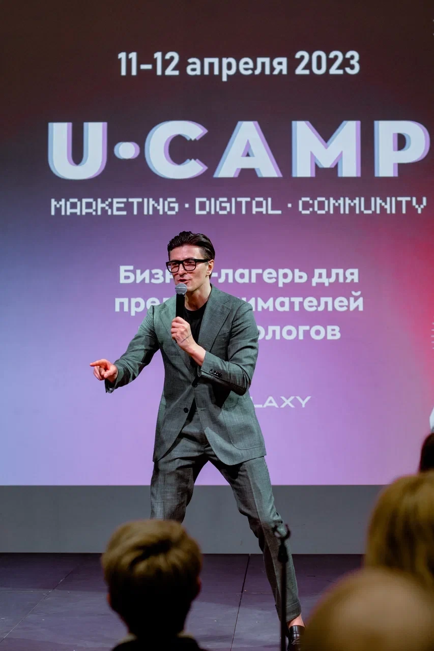 выступающий в очках жестикулирует на сцене конференции для предпринимателей
