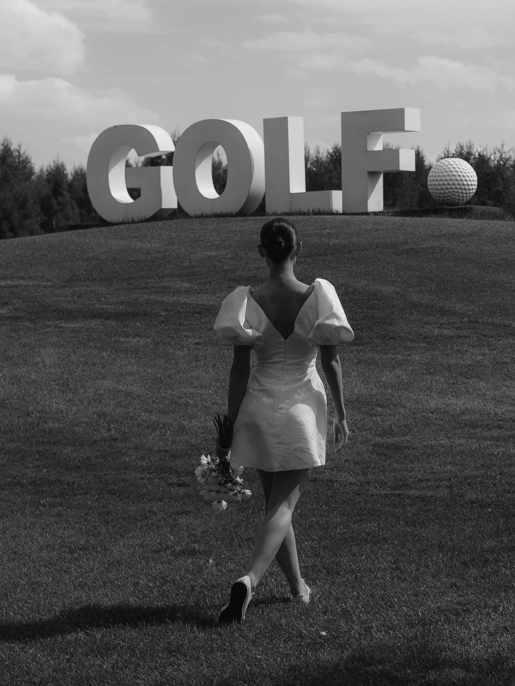 девушка в коротком платье идёт к скульптуре надписи GOLF
