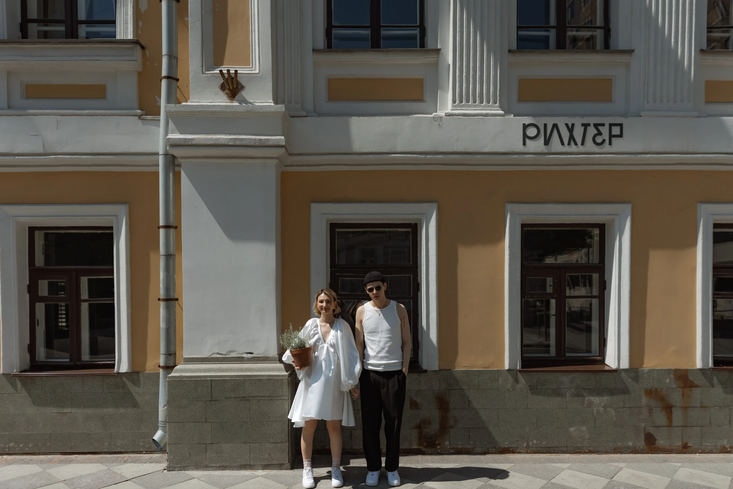 пара держится за руки у здания с вывеской на фасаде