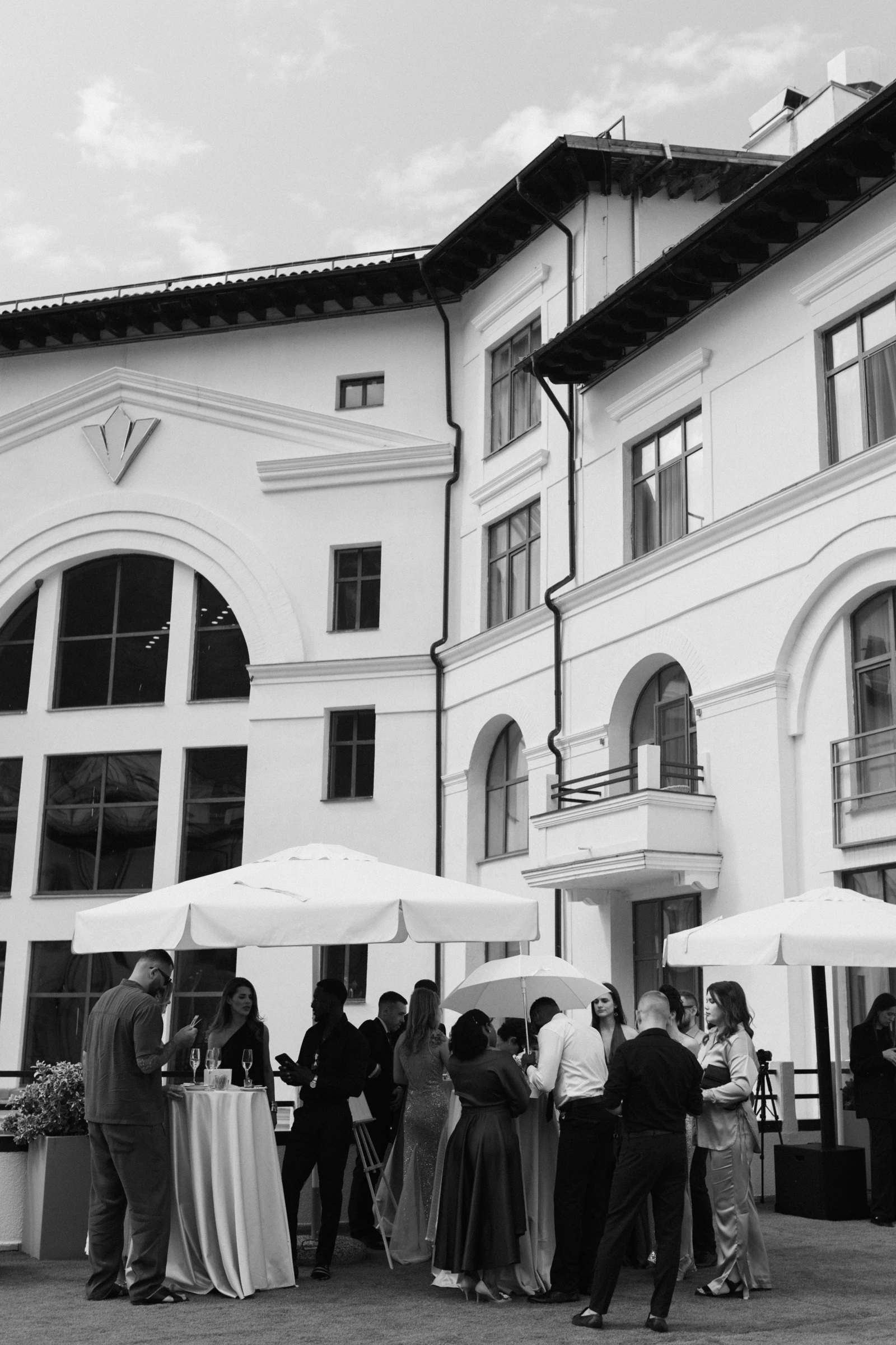 гости в вечерних нарядах стоят под зонтами у здания отеля