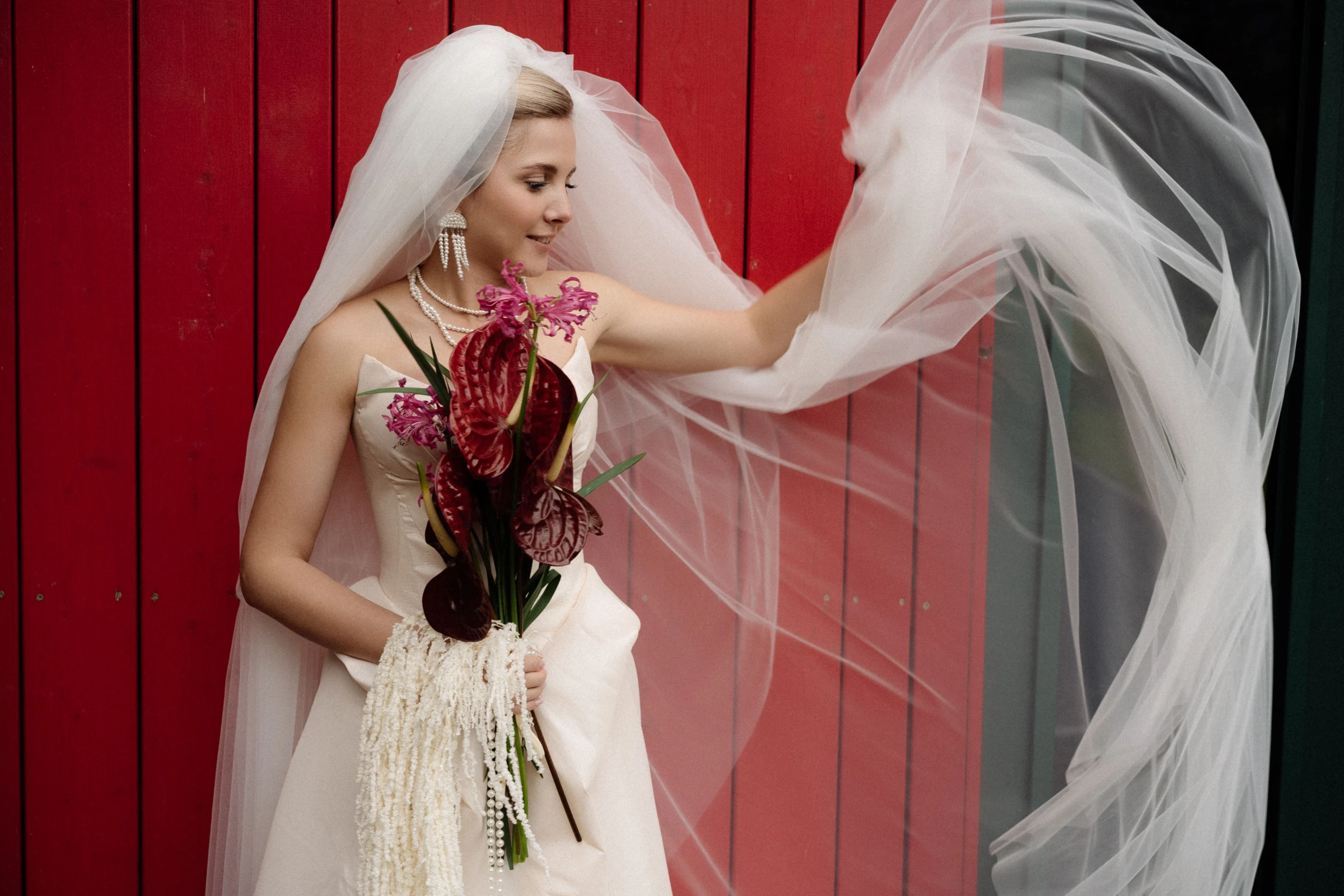 невеста с фатой на ветру держит бордовый букет антуриумов