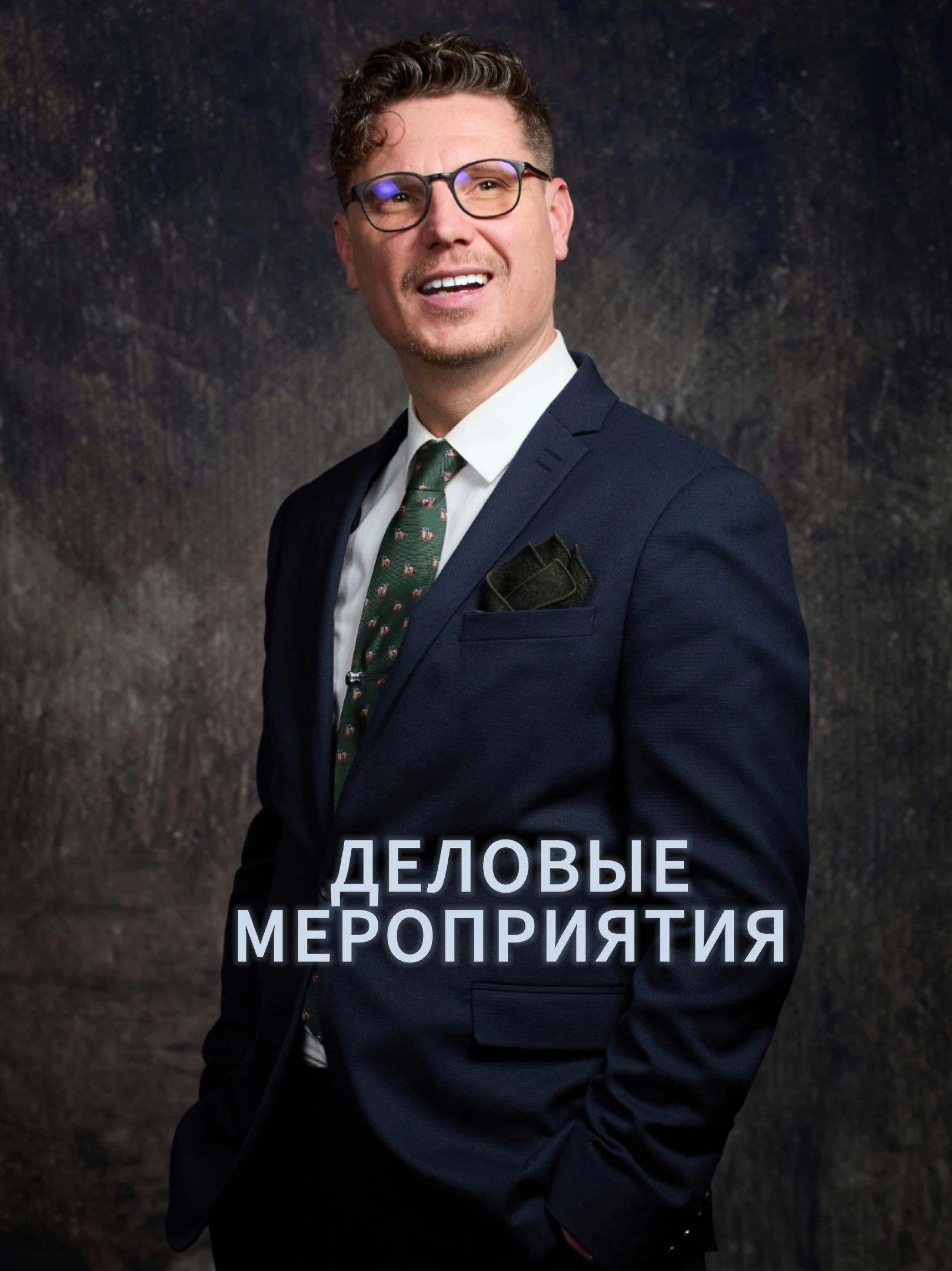 мужчина в очках и синем костюме улыбается на тёмном фоне