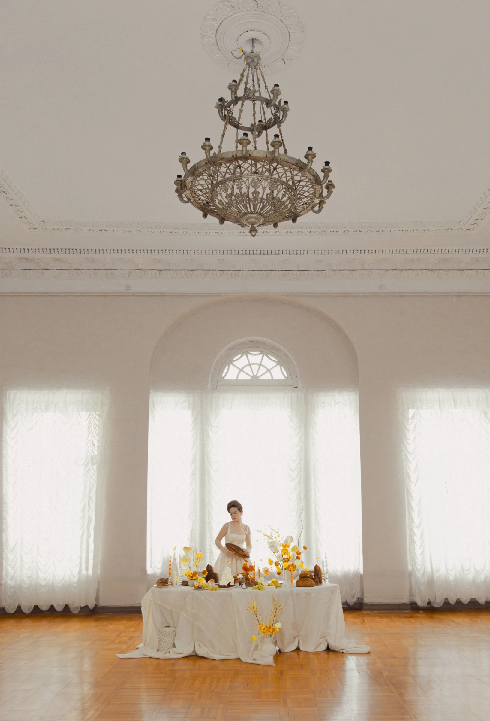 женщина сервирует круглый стол в старинном зале с люстрой