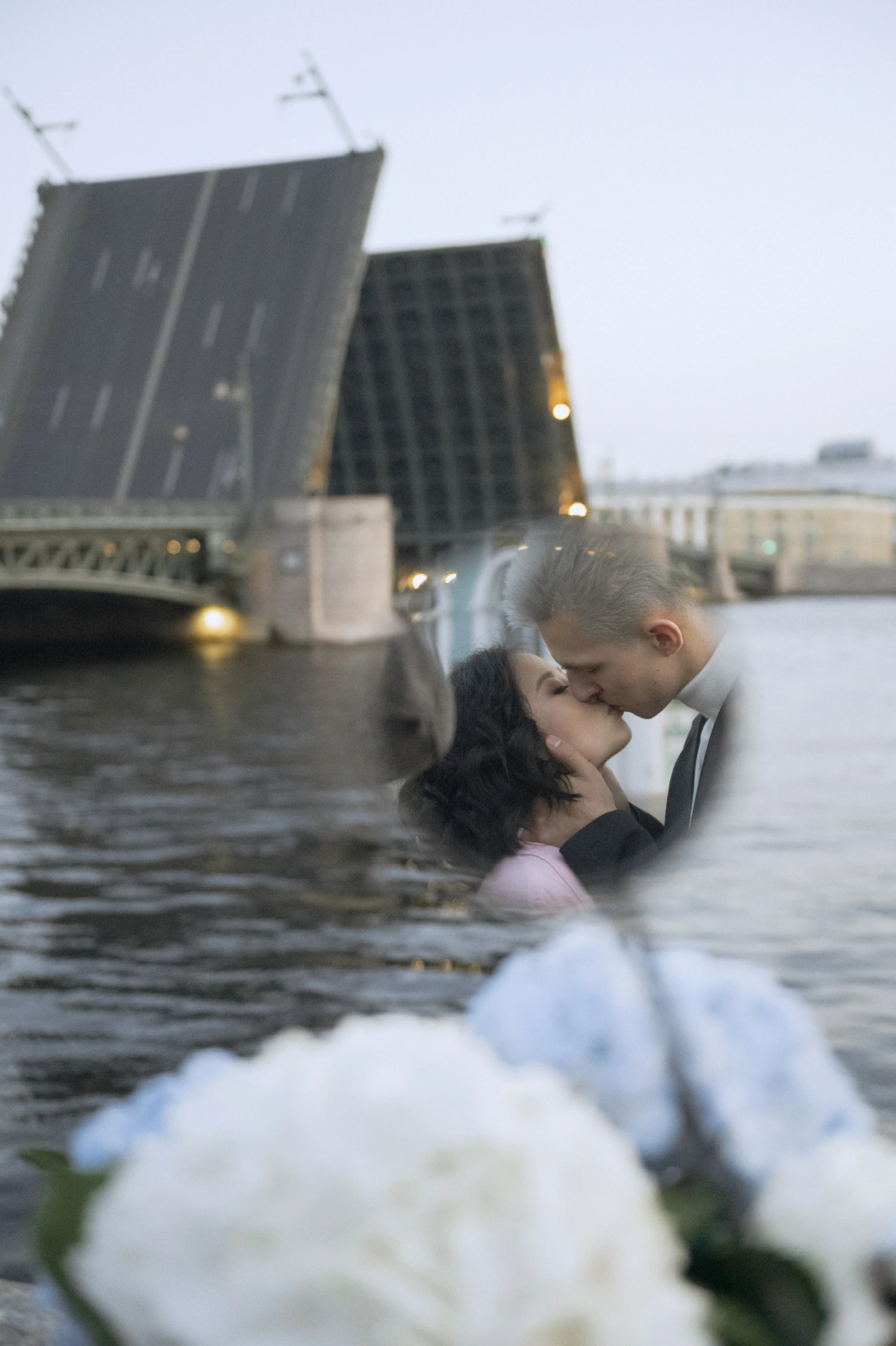 пара целуется в воде на фоне разведённого моста вечером в городе