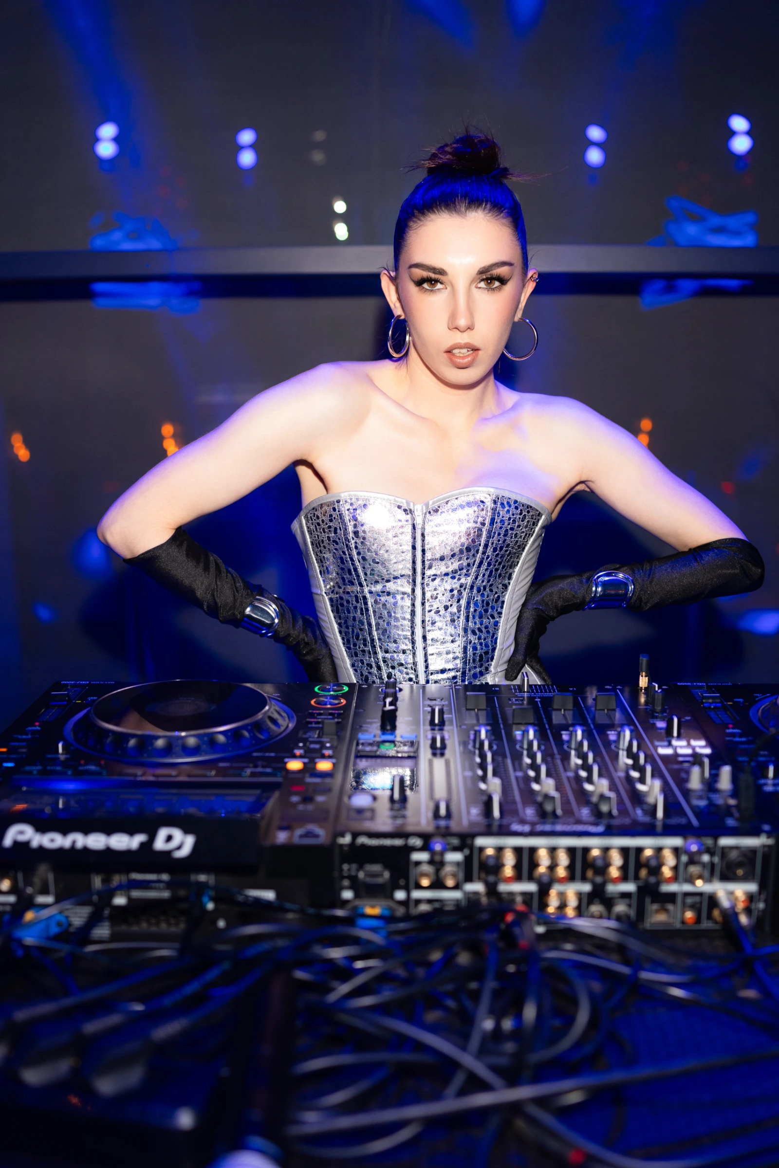 диджей в серебристом корсете стоит за пультом Pioneer DJ вечером