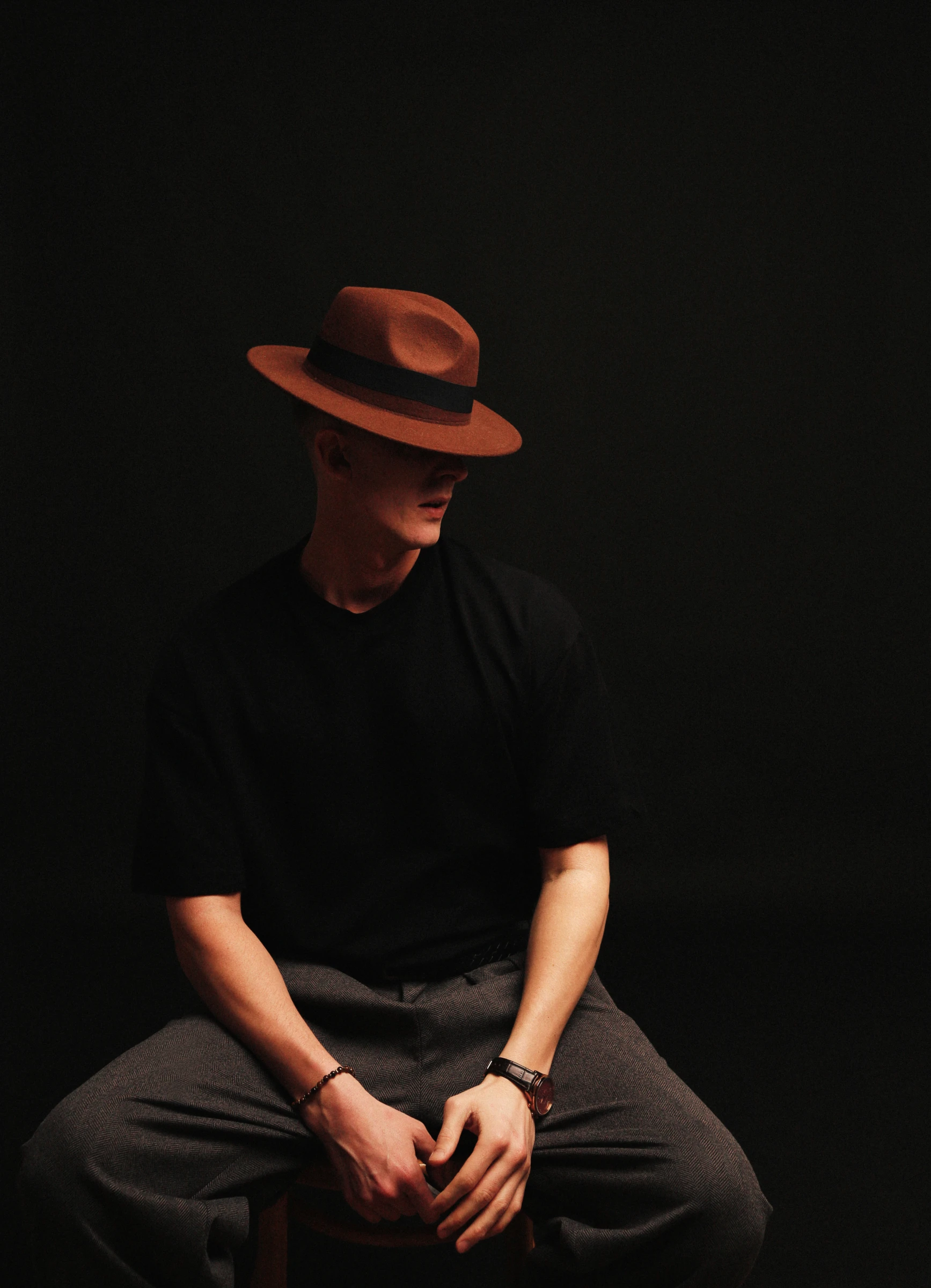 ведущий свадеб в коричневой шляпе сидит вполоборота на тёмном фоне