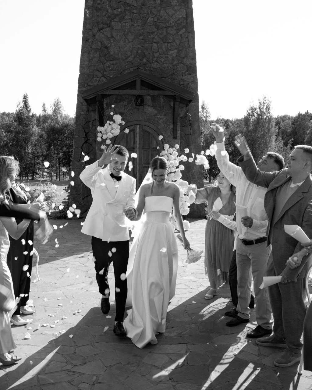 молодожёны идут под лепестками роз у каменной башни