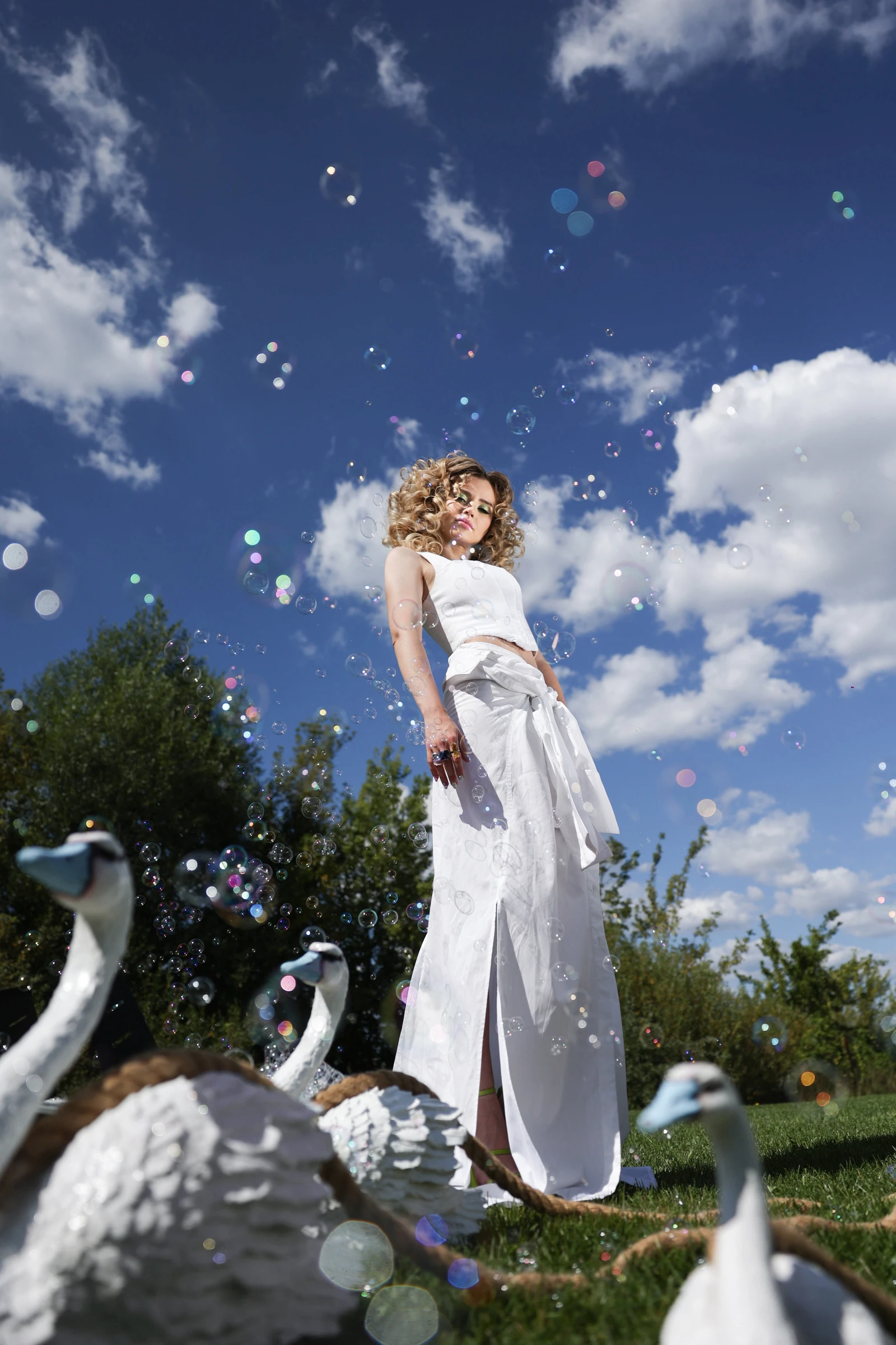 невеста в белом костюме среди декоративных лебедей и мыльных пузырей