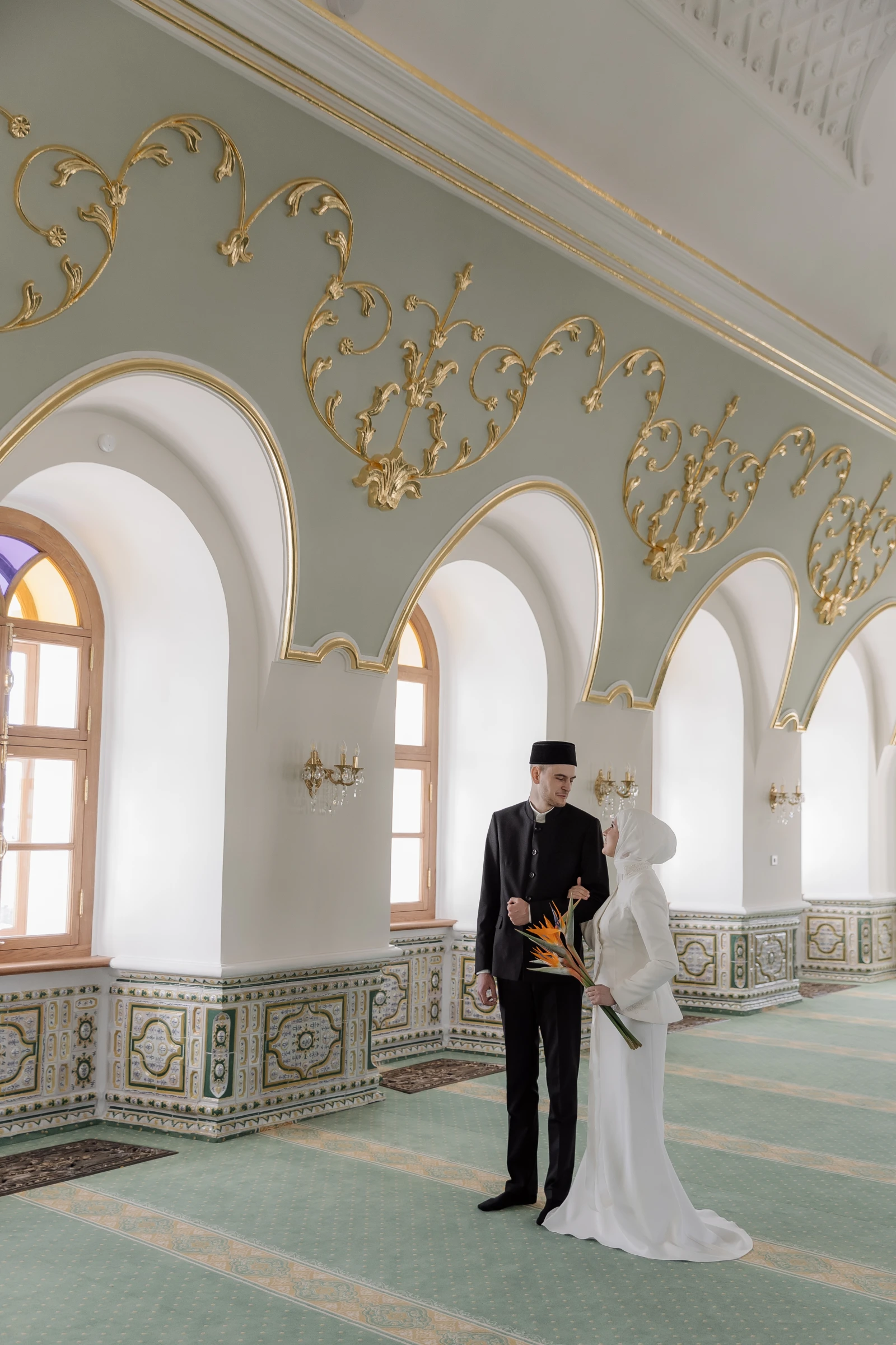 пара стоит под арками зала с золотой лепниной и букетом стрелиций