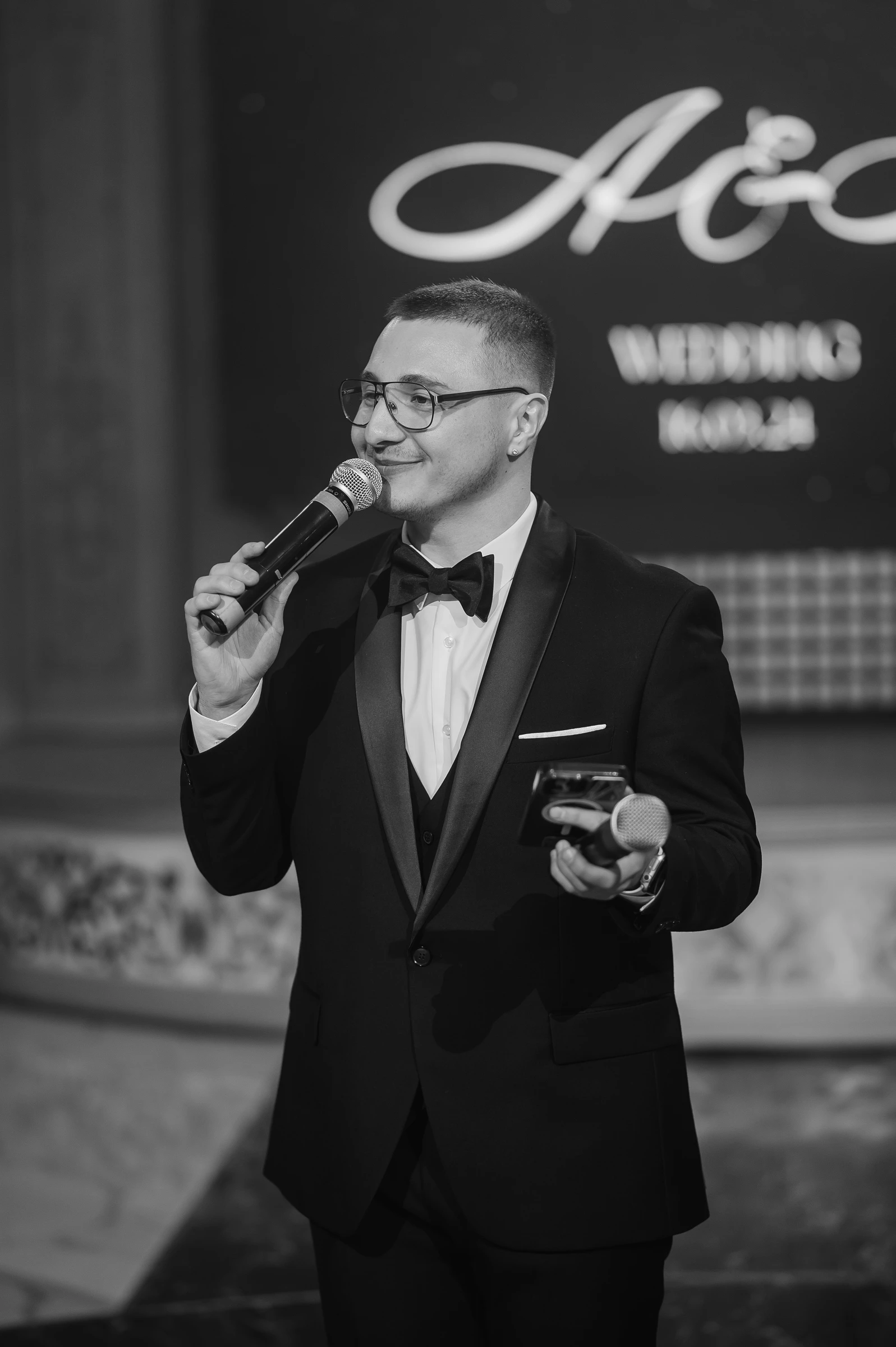 ведущий в смокинге с микрофоном на фоне надписи wedding day