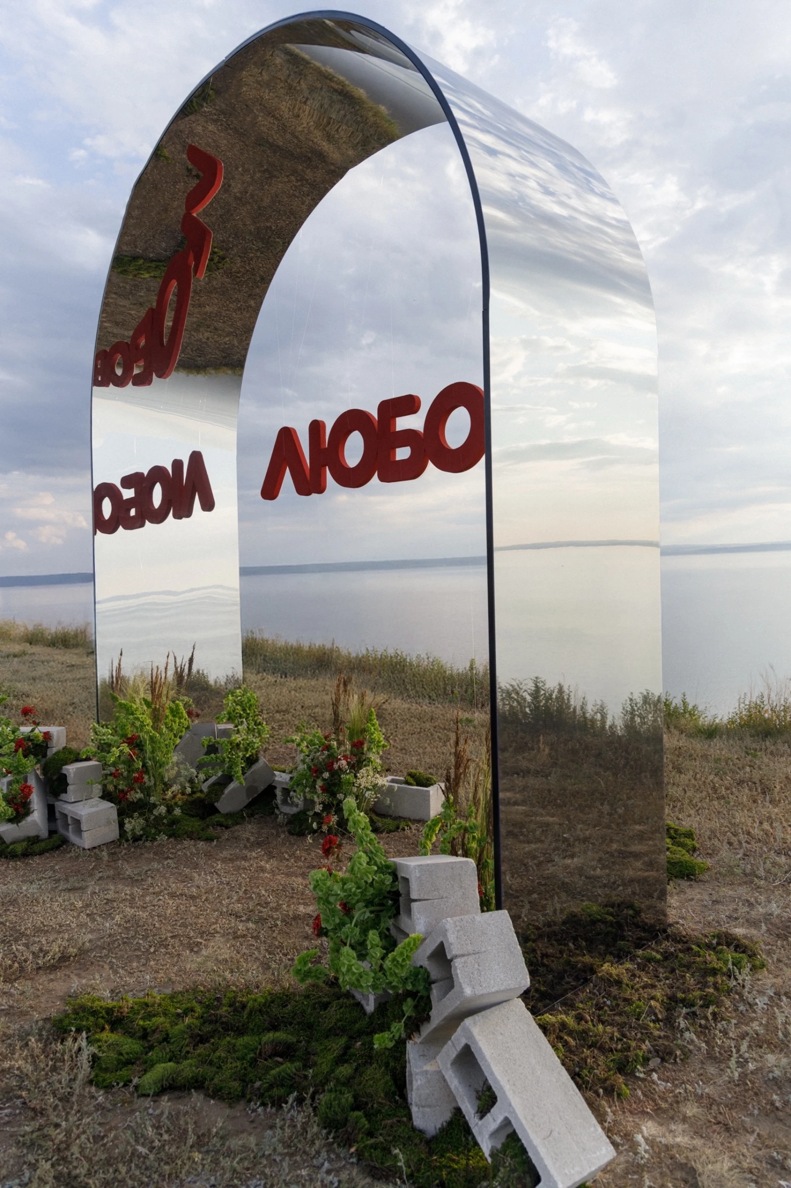 Зеркальная арка с надписью Любовь среди клумб из бетонных блоков у озера