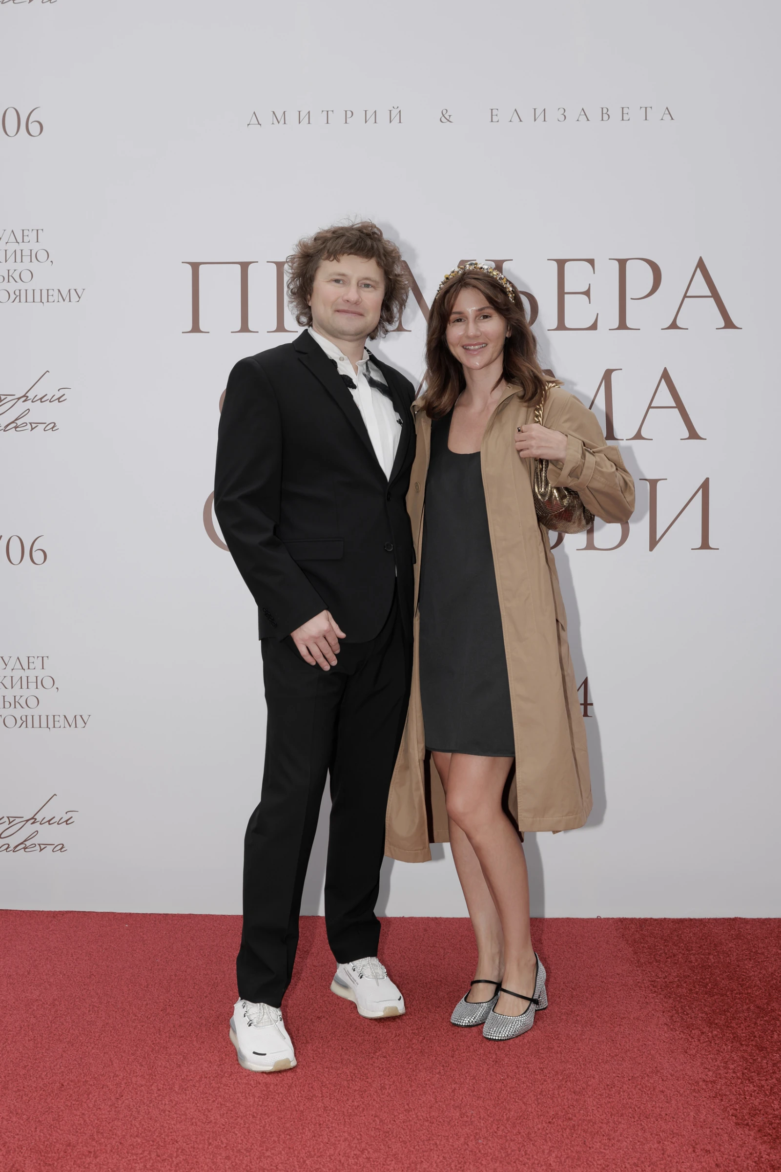 Женщина в сером пальто держит бокал шампанского у баннера