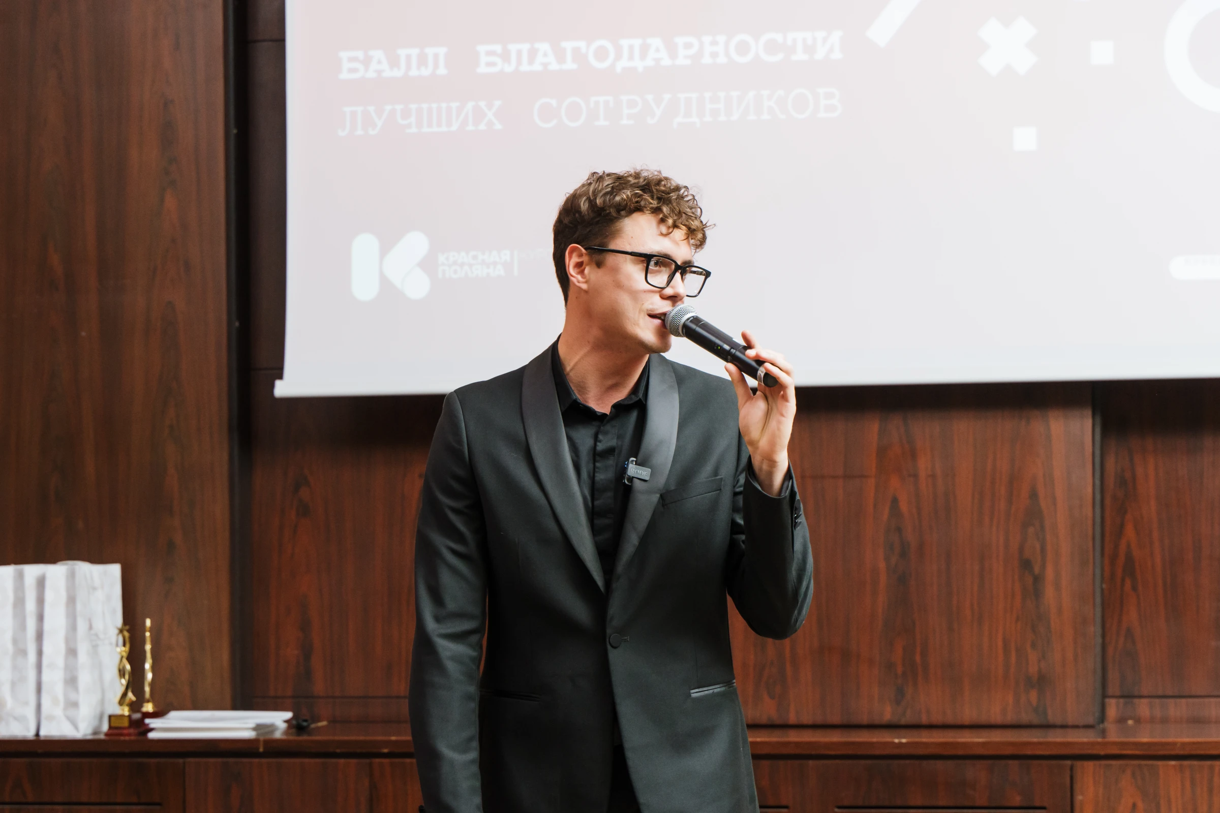 мужчина с микрофоном выступает на сцене корпоративного мероприятия с наградой