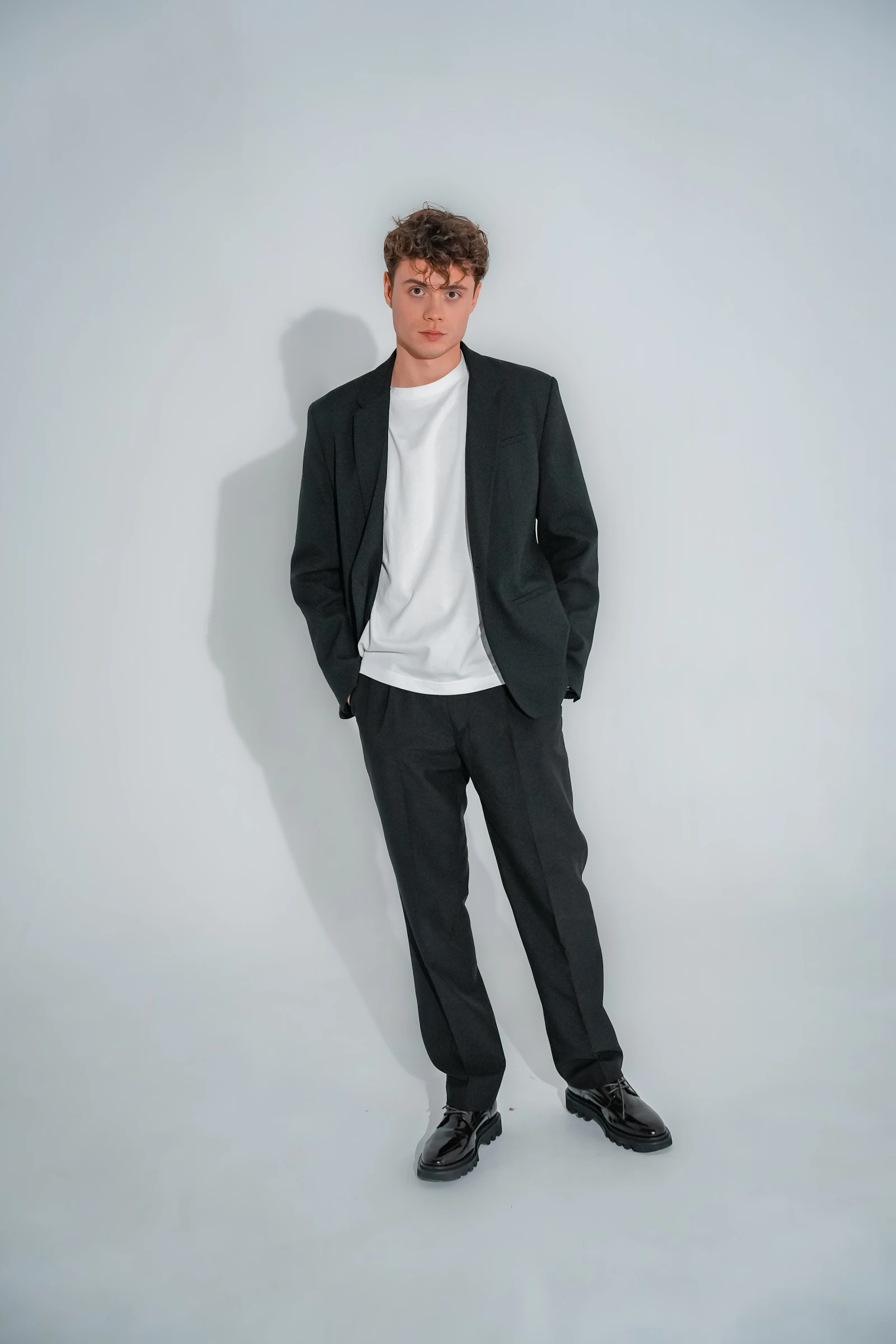 мужчина в чёрном костюме и белой футболке студийный портрет в рост