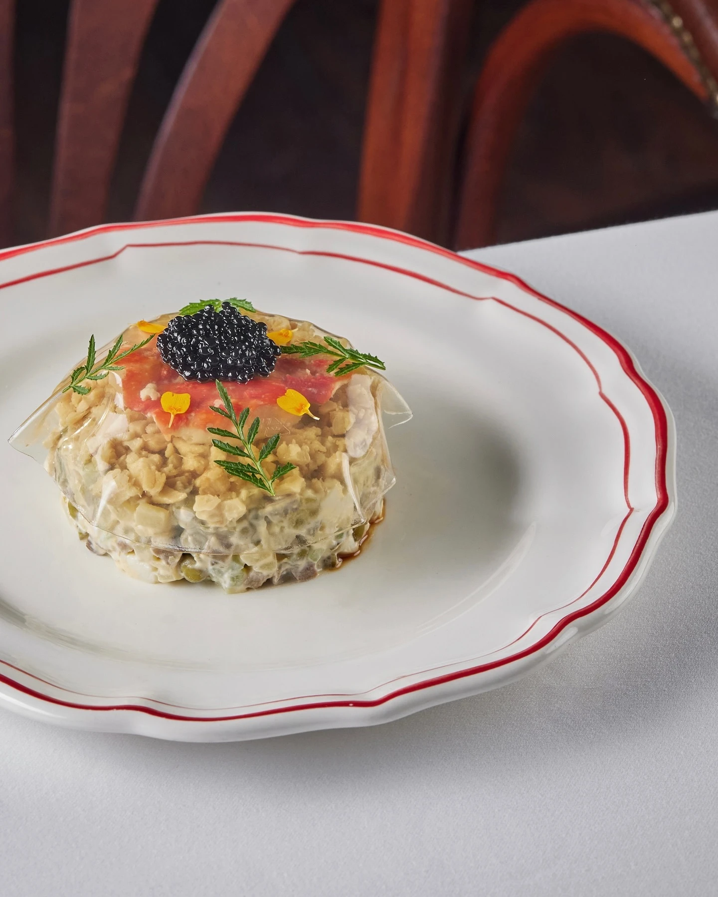 Слоёный салат с чёрной икрой и томатом на тарелке с красной каёмкой