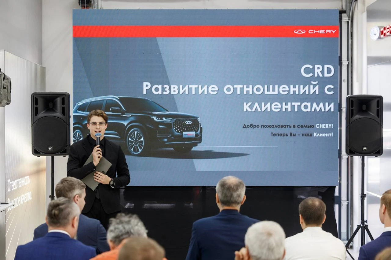 ведущий у экрана с презентацией программы CRD Chery