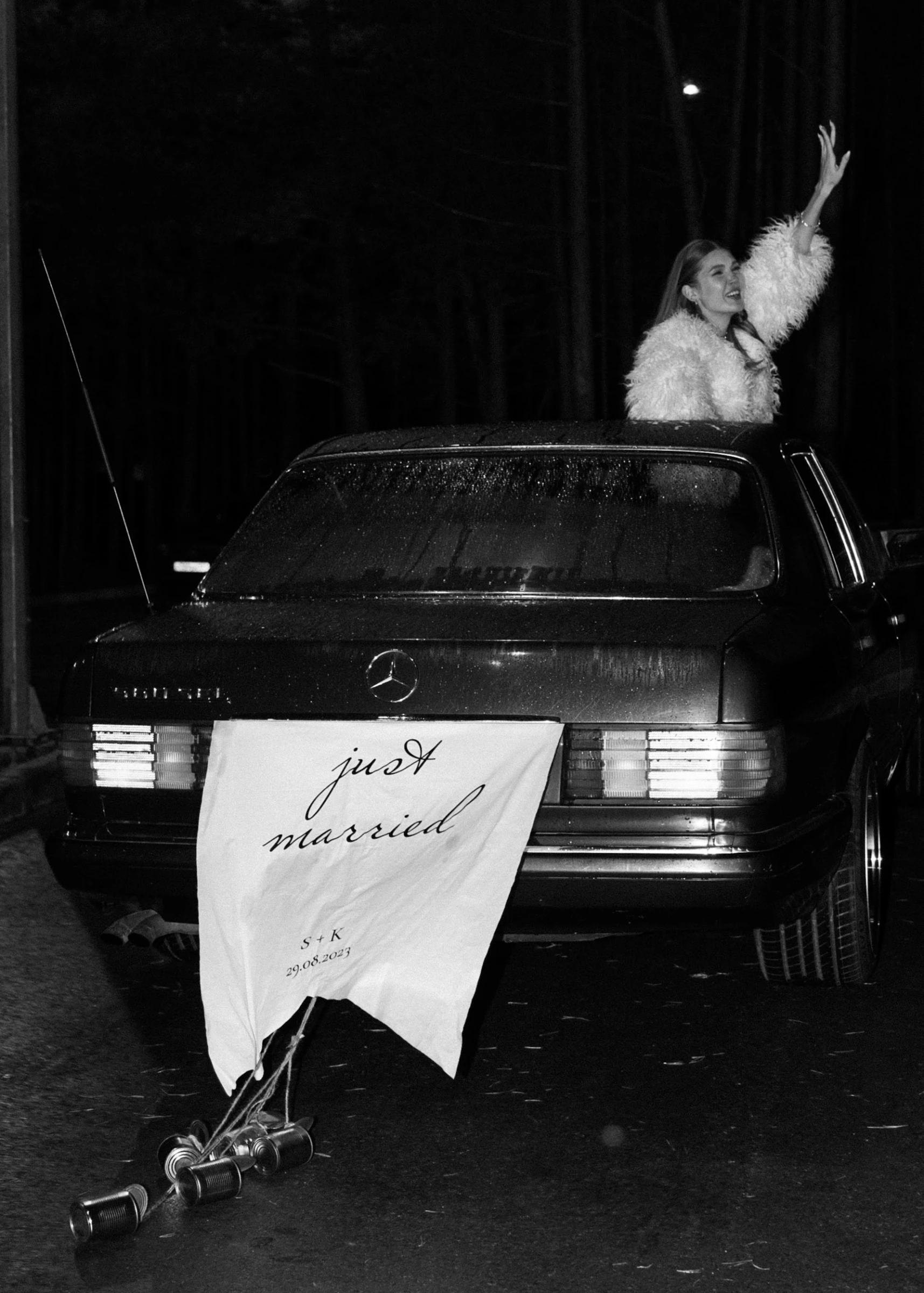 Невеста машет рукой из люка ретроавтомобиля с табличкой Just Married