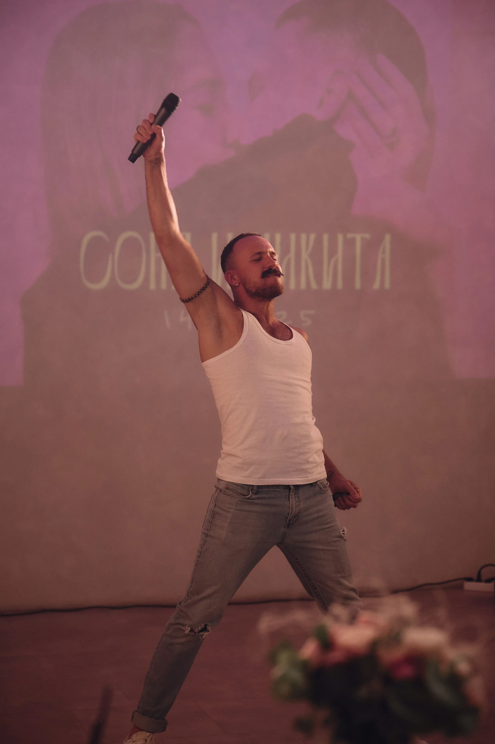 Ведущий поднимает микрофон на сцене на фоне проекции с именами молодожёнов