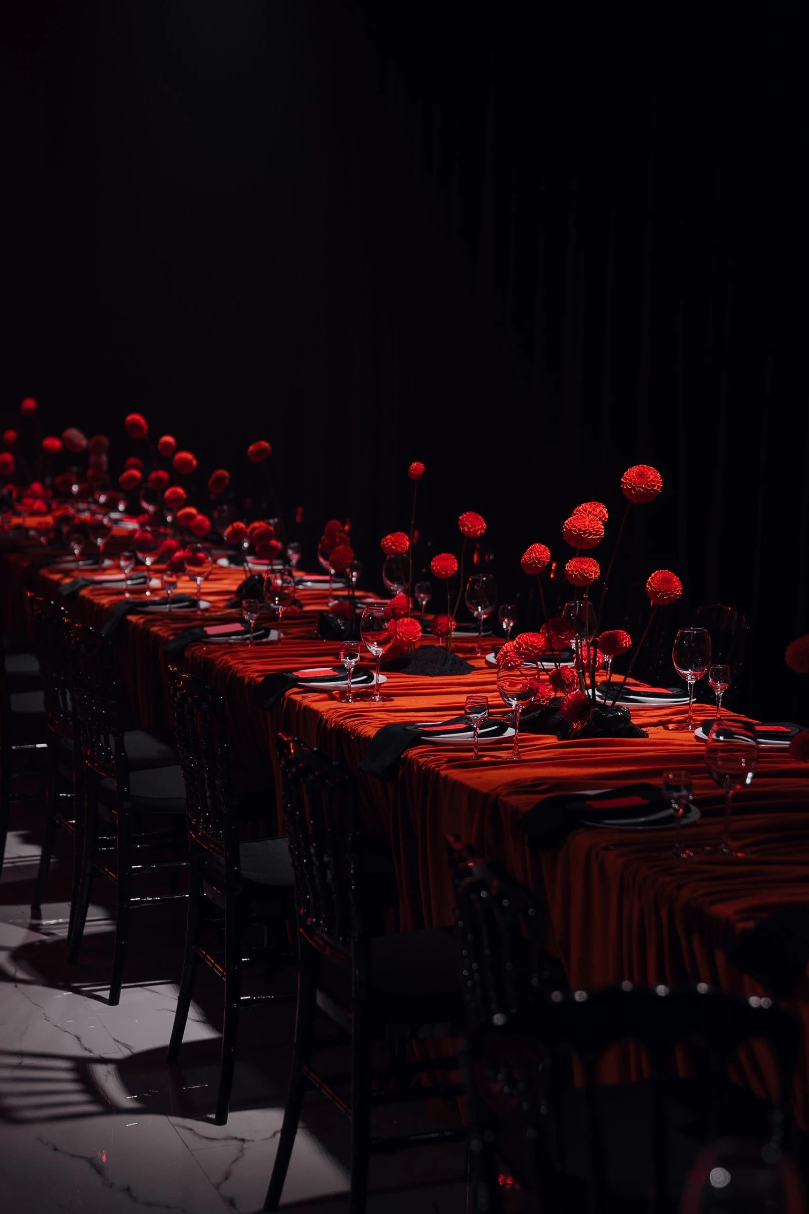 длинный банкетный стол с оранжевой скатертью и алыми цветами в темном зале