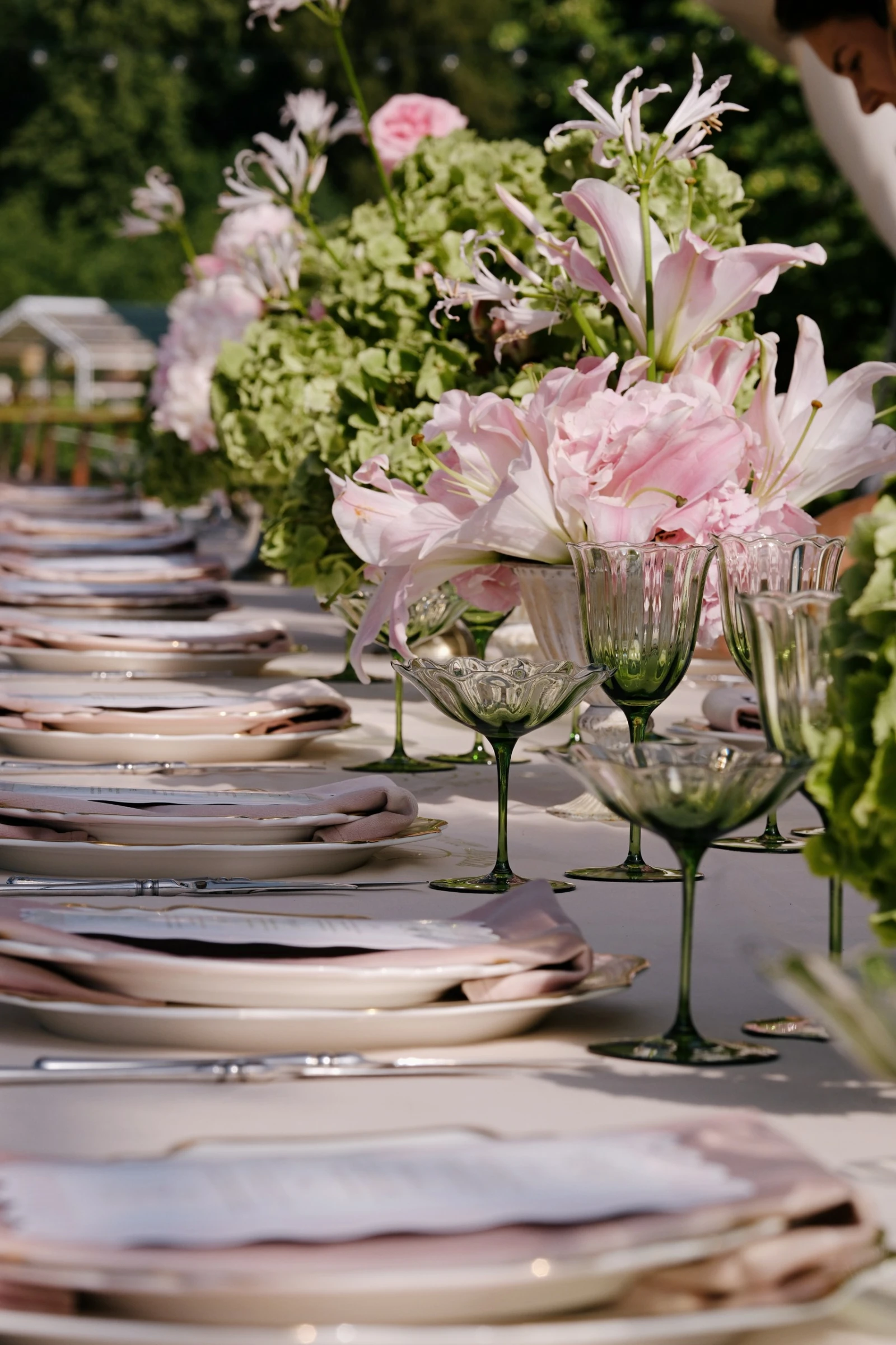 Ряд сервированных тарелок и зелёных бокалов вдоль стола с розовыми лилиями