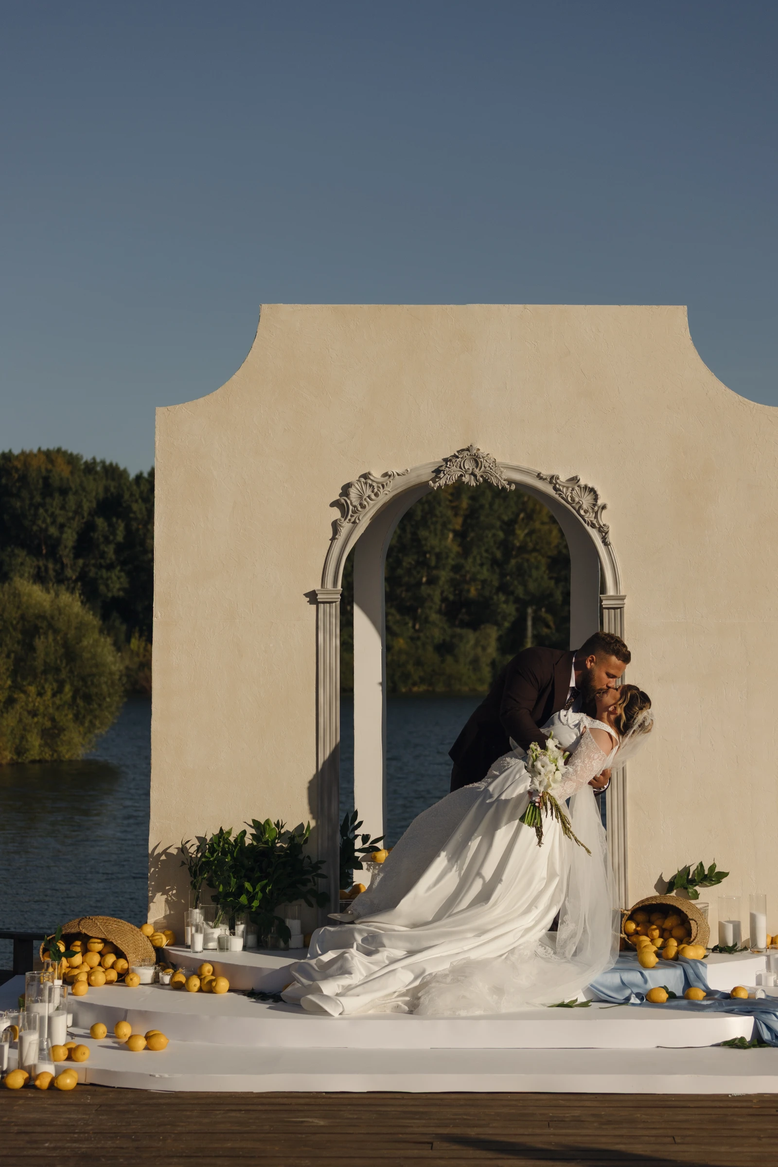 жених целует невесту с букетом у декоративной арки с корзинами лимонов