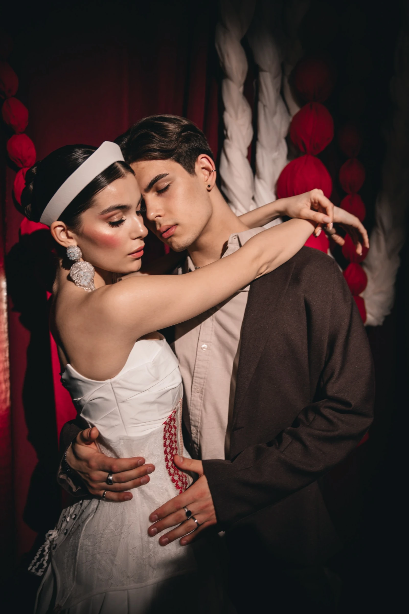 невеста в белом корсете обнимает жениха на фоне красного декора и гирлянд
