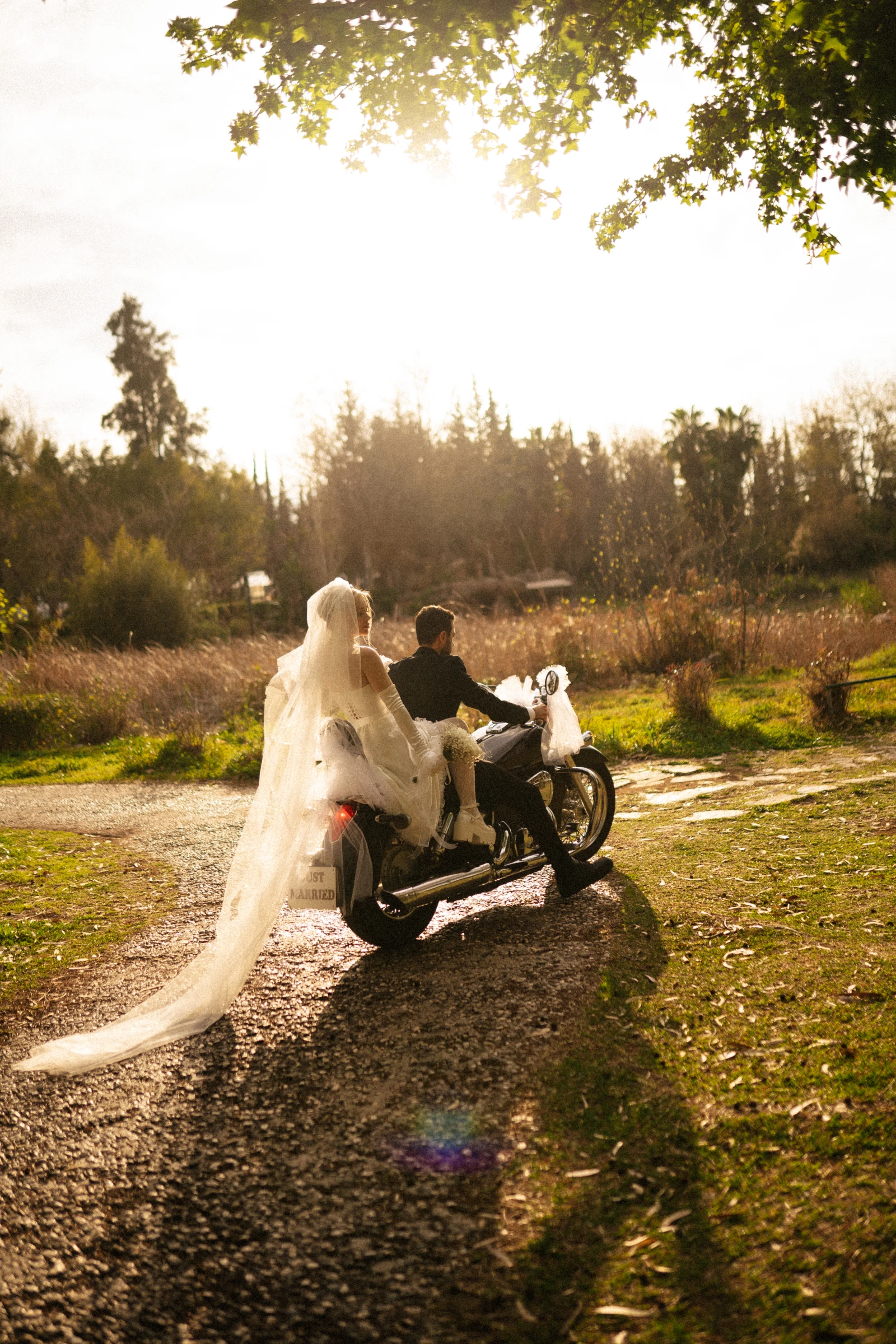 невеста в длинной фате едет с женихом на винтажном мотоцикле с табличкой just married