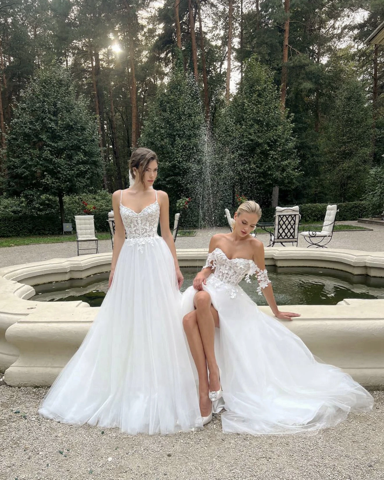 две невесты в кружевных платьях у каменного фонтана в парке