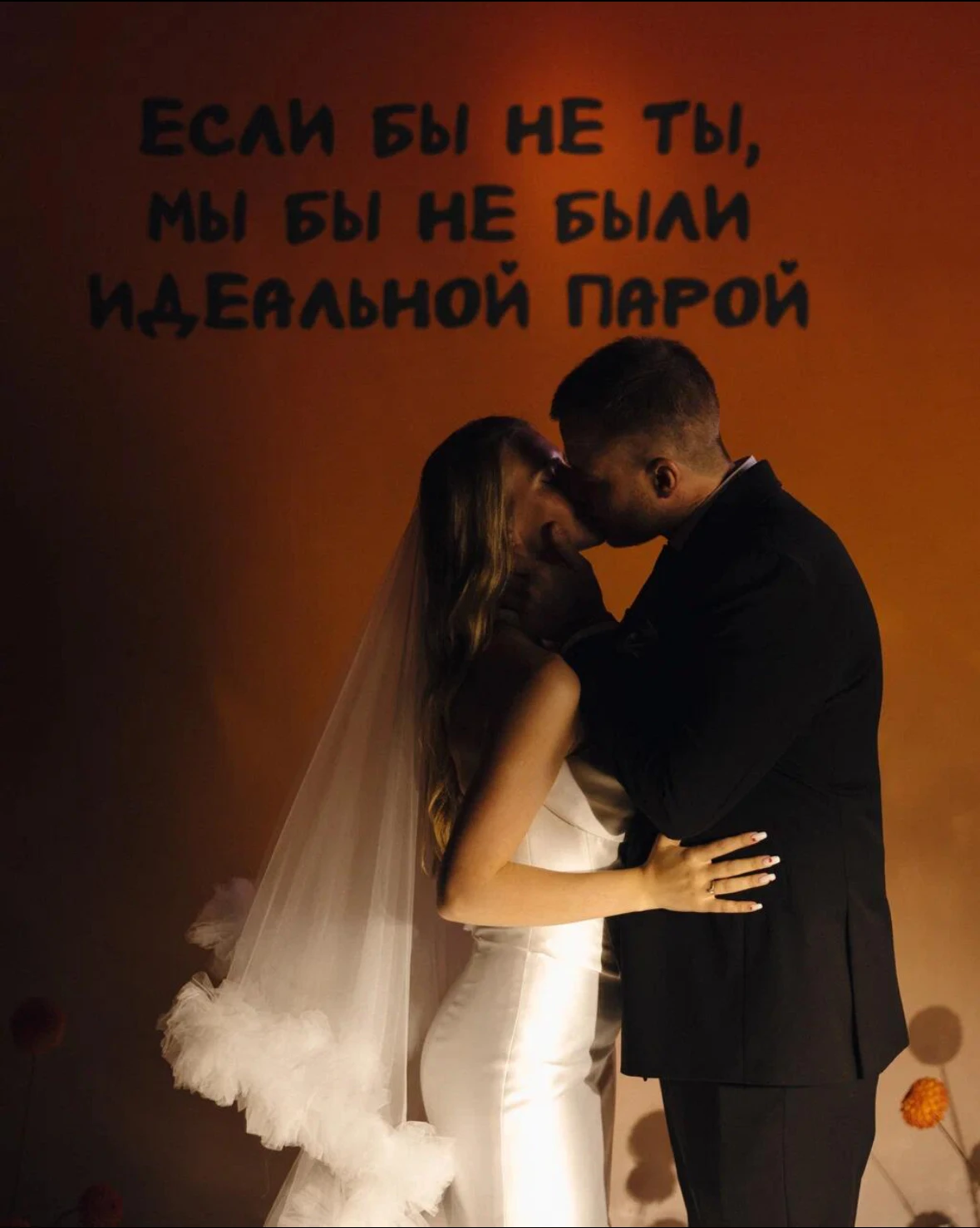 поцелуй молодожёнов на фоне оранжевой подсветки с надписью на стене
