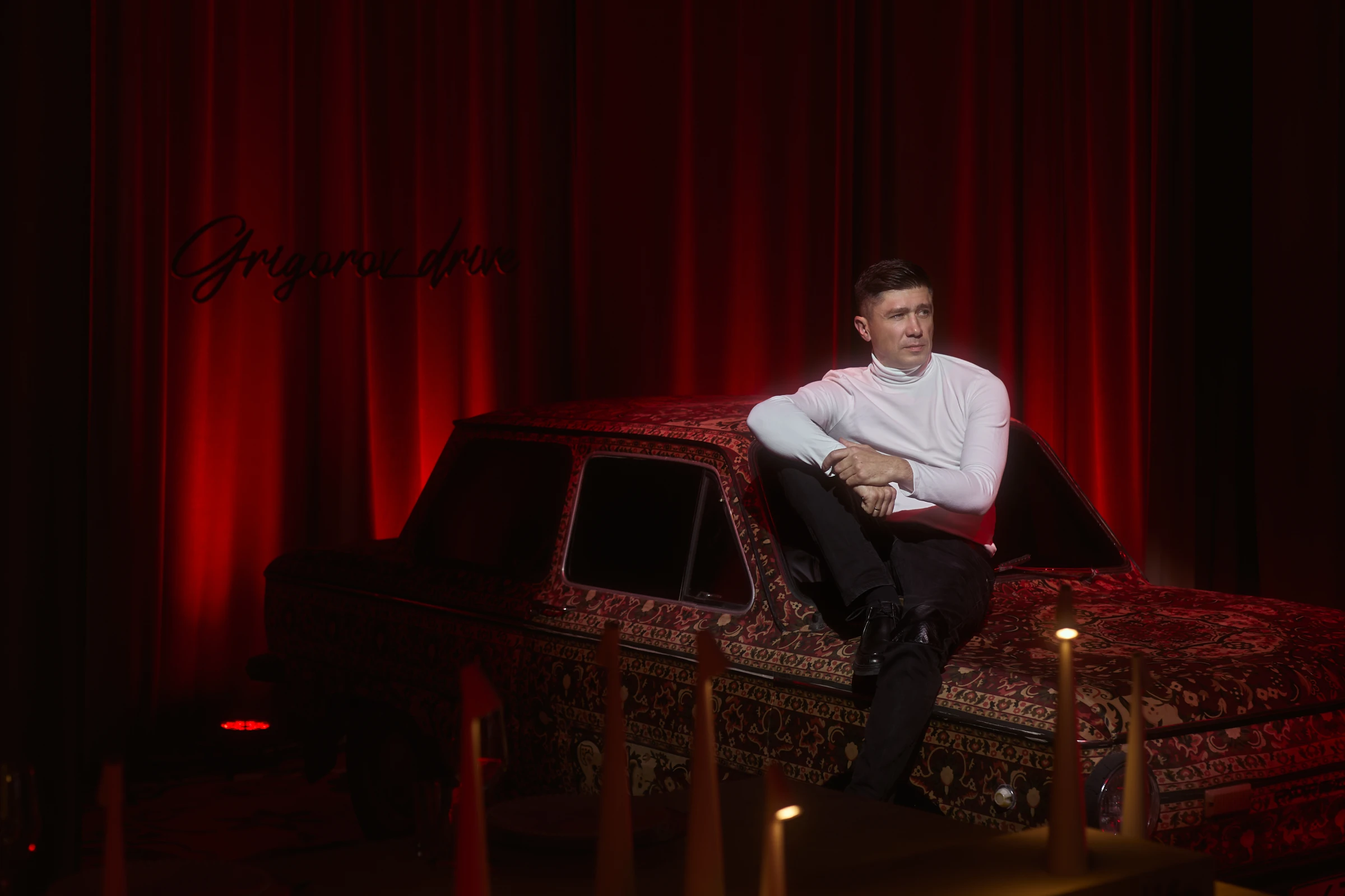 ведущий сидит на декорированном автомобиле в красном интерьере со свечами