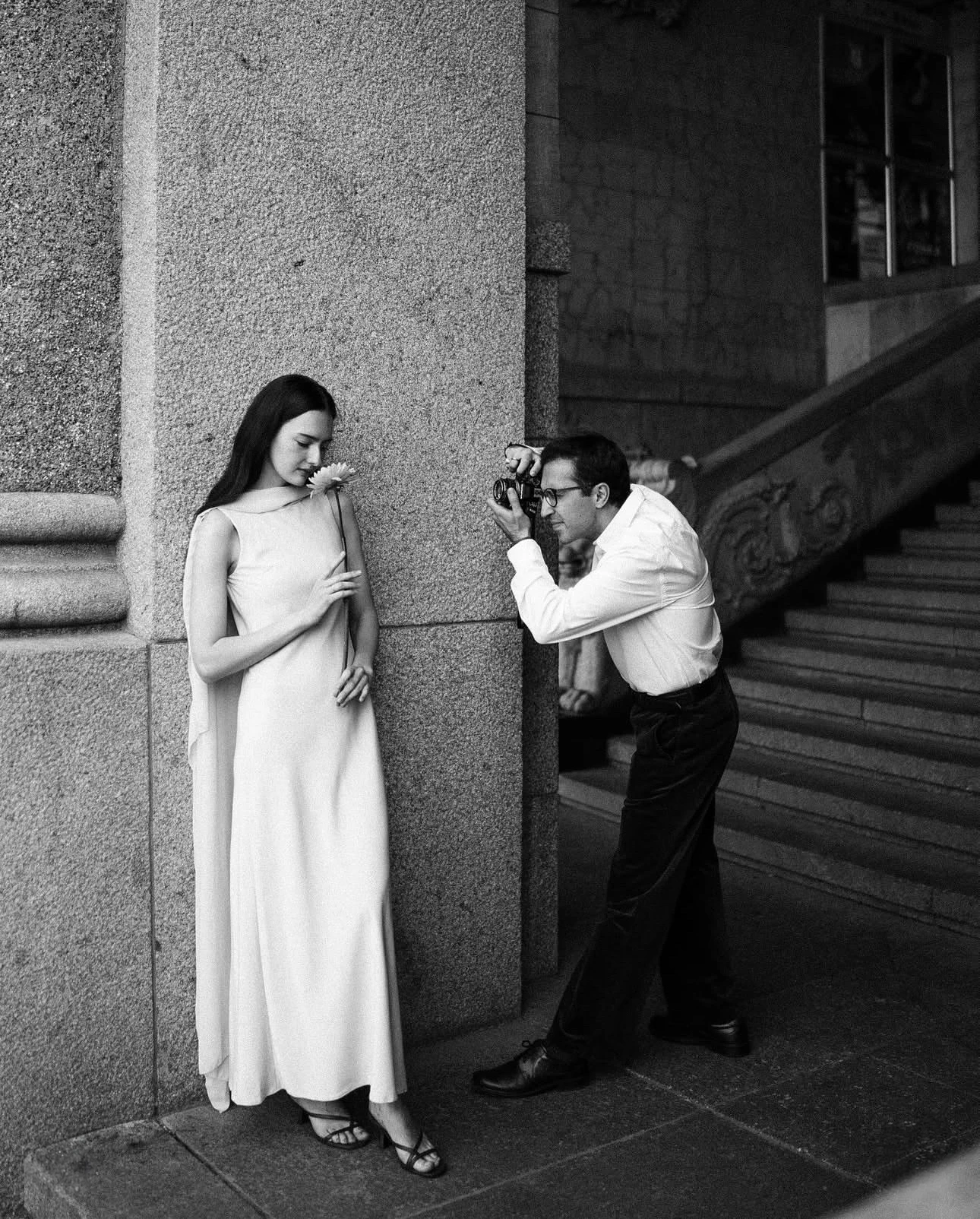 фотограф снимает невесту с цветком у каменной колонны здания