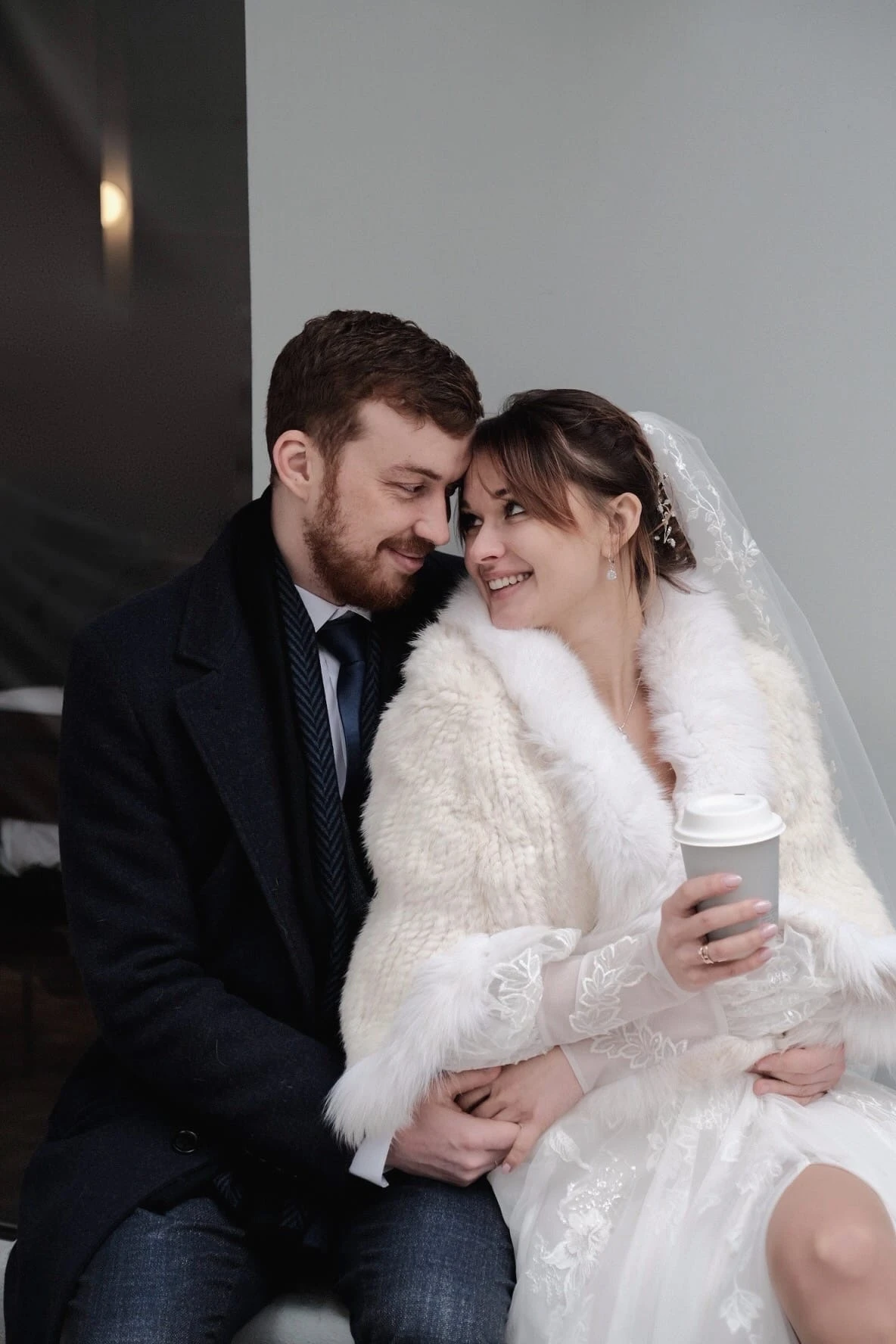 невеста в белой меховой накидке с кофе улыбается жениху зимним днём